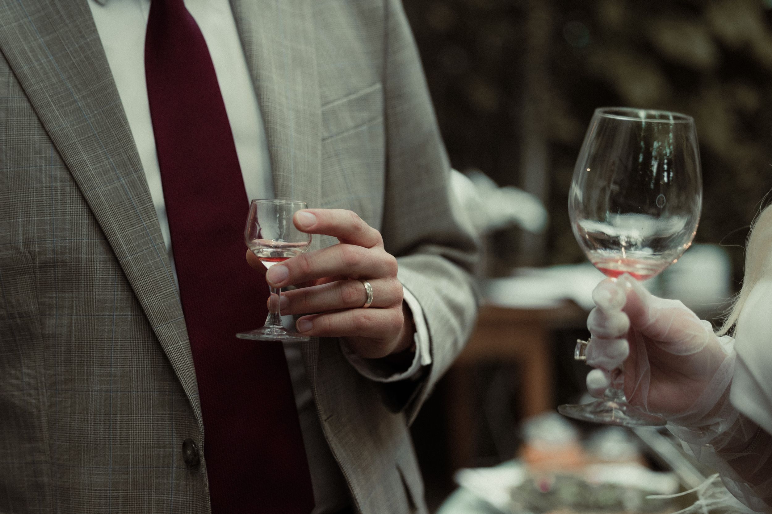 Person wearing a gray suit and burgundy tie holds a wine glass at a formal event setting.