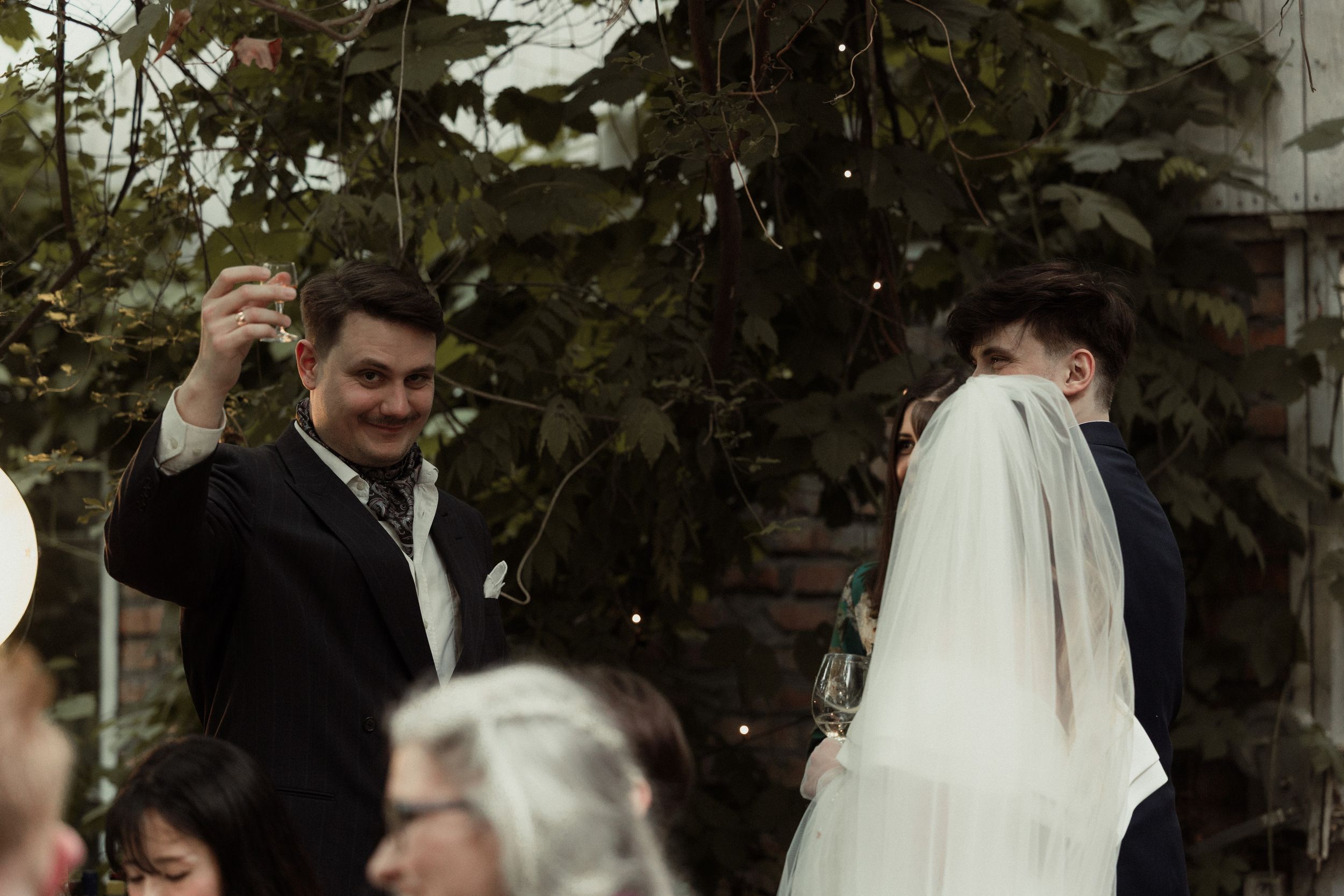A couple celebrating their wedding ceremony outdoors surrounded by greenery and guests.