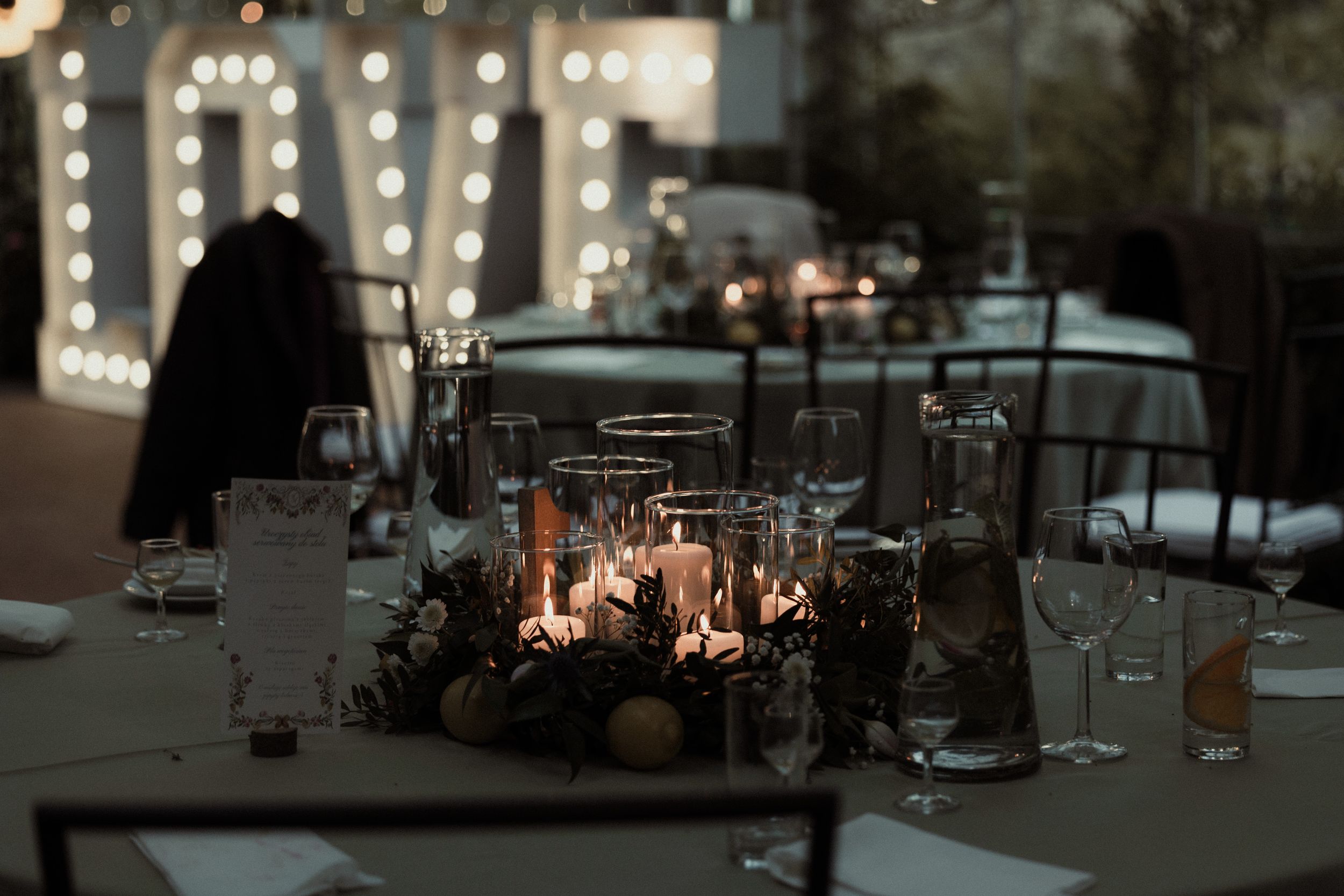Romantic candlelit table setting at dusk with glowing LOVE sign illuminated in background.