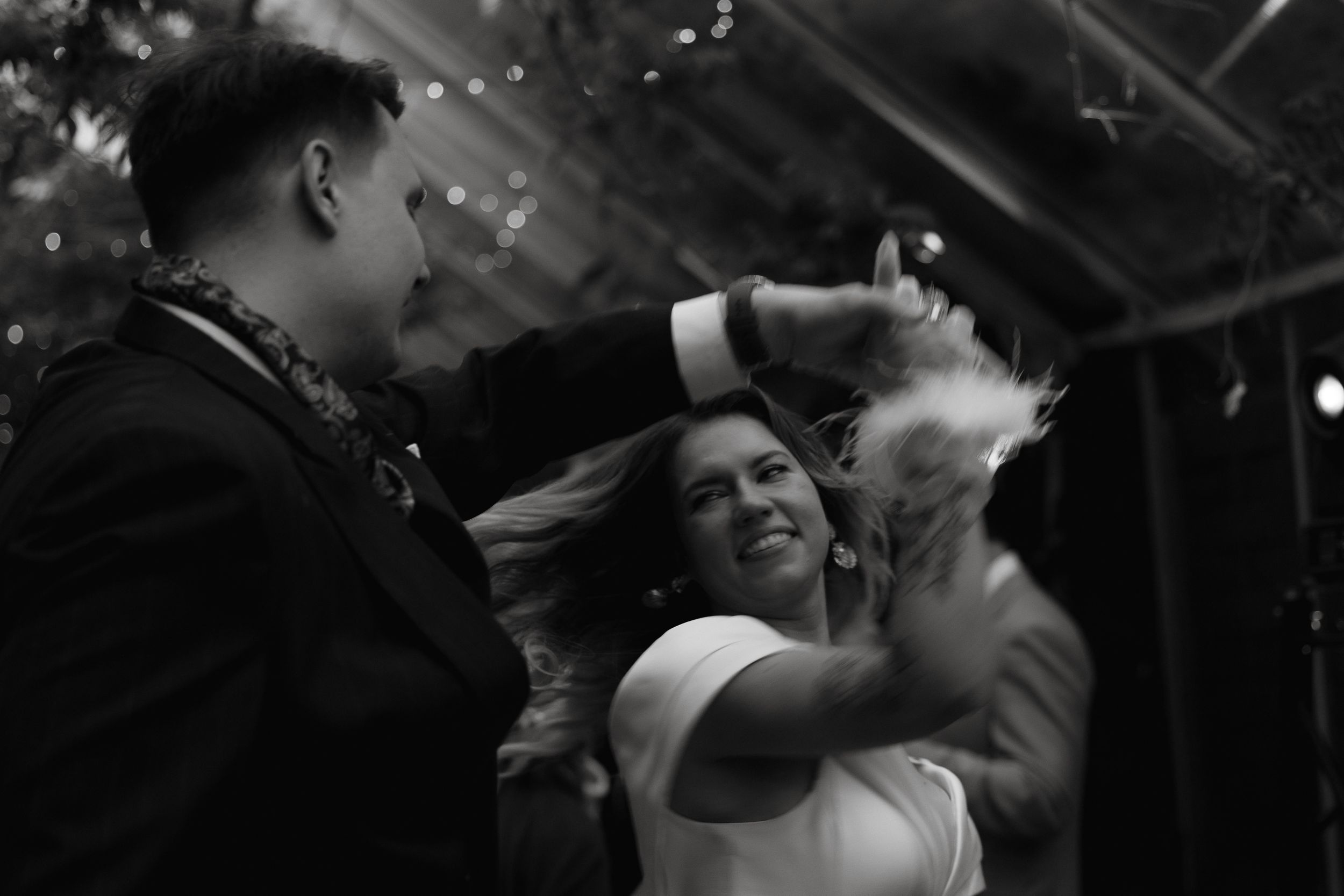 Black and white candid photo of a couple dancing together and smiling at their wedding celebration.