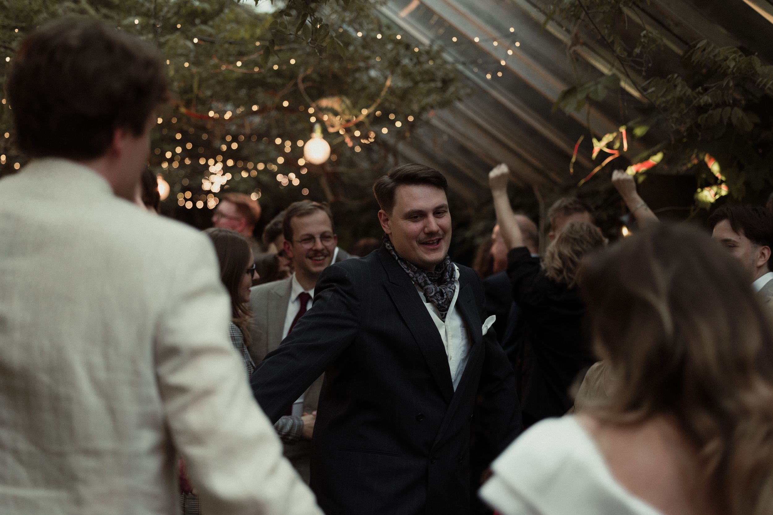 Reception guests dancing and celebrating under twinkling lights at an indoor evening wedding venue.