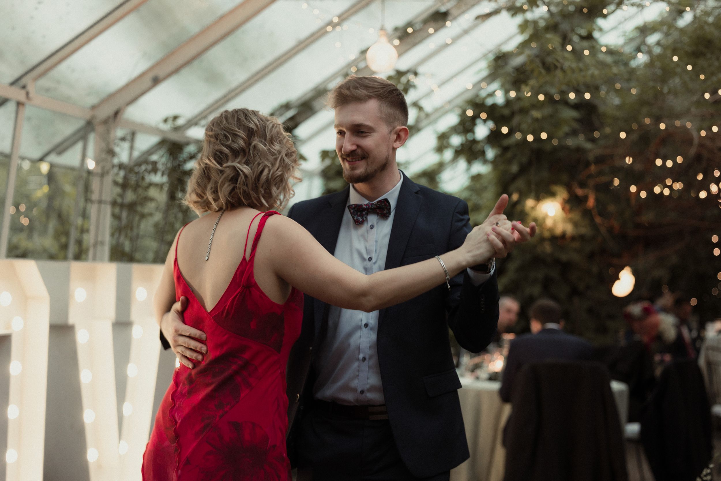 Couple dancing together at an evening wedding reception in a clear tent with string lights overhead.