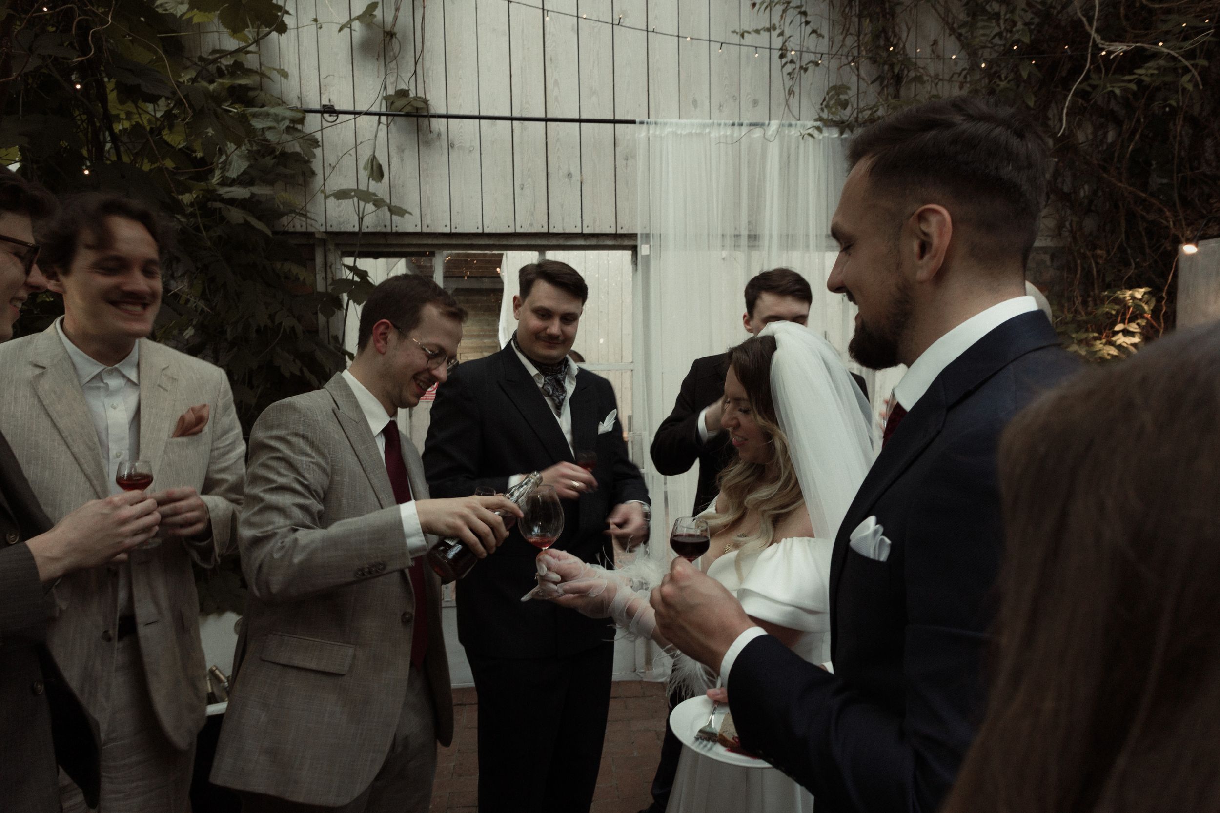 Guests at a wedding reception share celebratory moments in dark formal attire and suits.