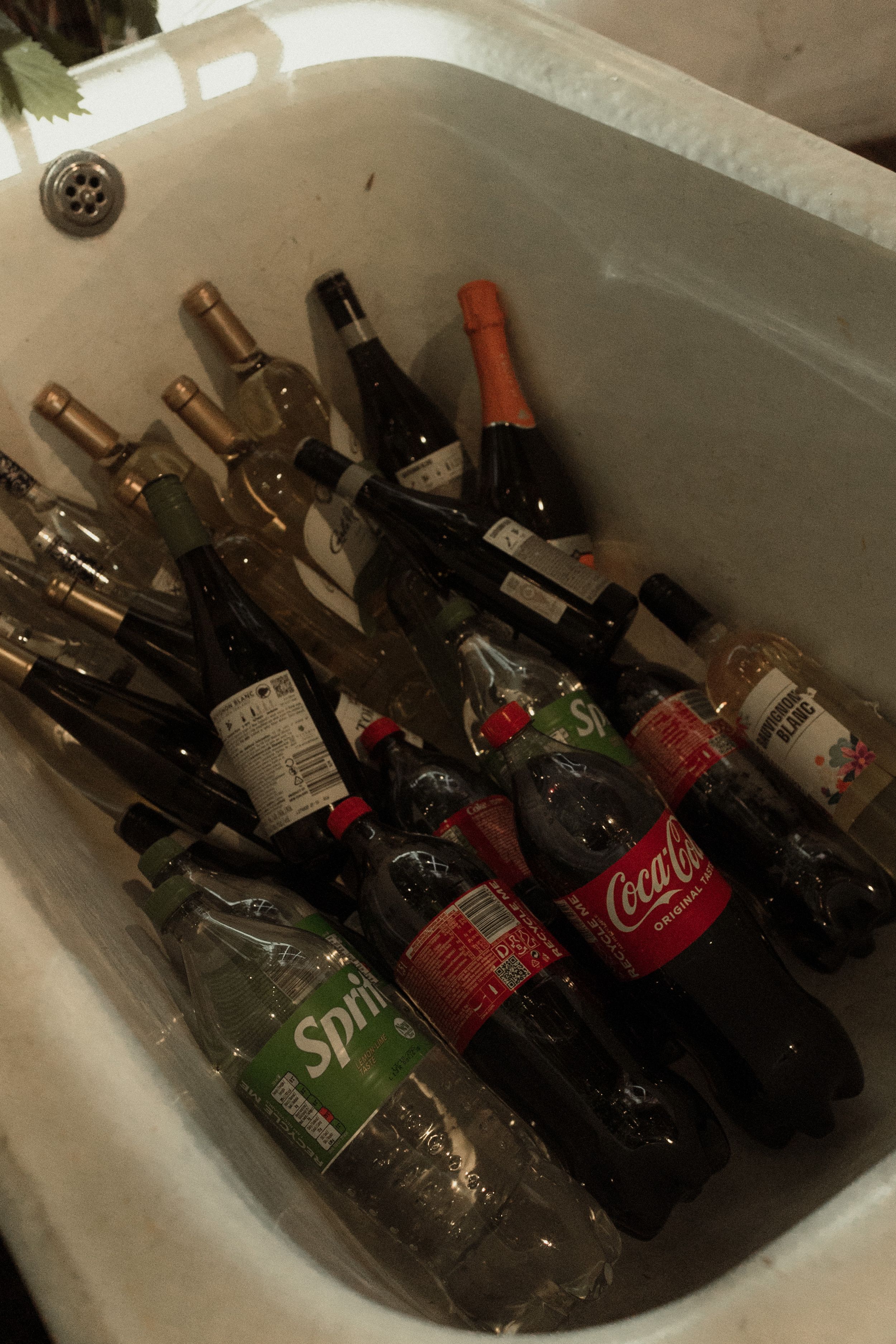 Assorted bottles of soda and beverages chilling in an ice-filled bathtub.