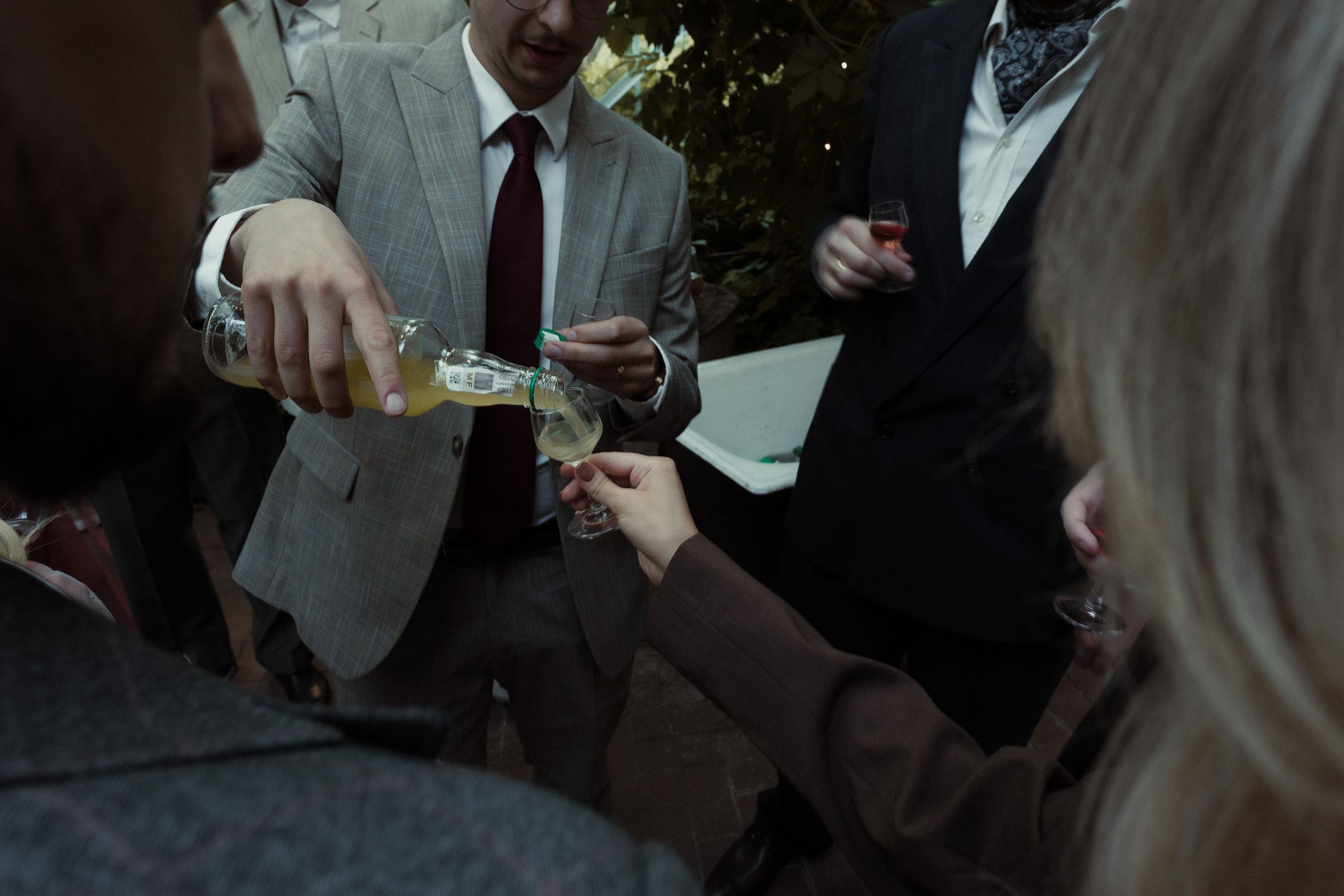 Group of people stand together outdoors in formal attire with beverages in their hands during a social gathering.