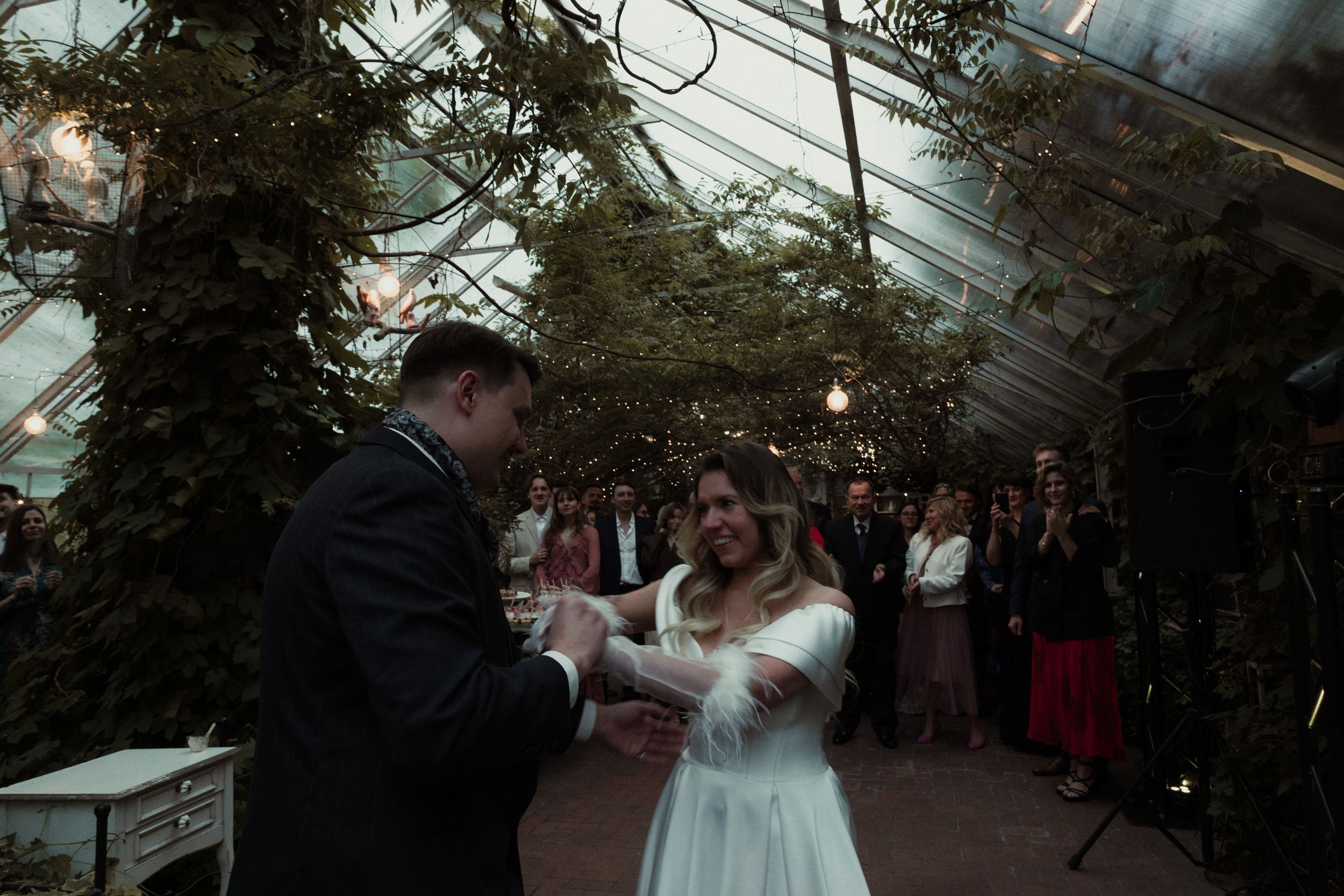 Guests enjoying a wedding celebration under a tent with string lights and greenery decorations.