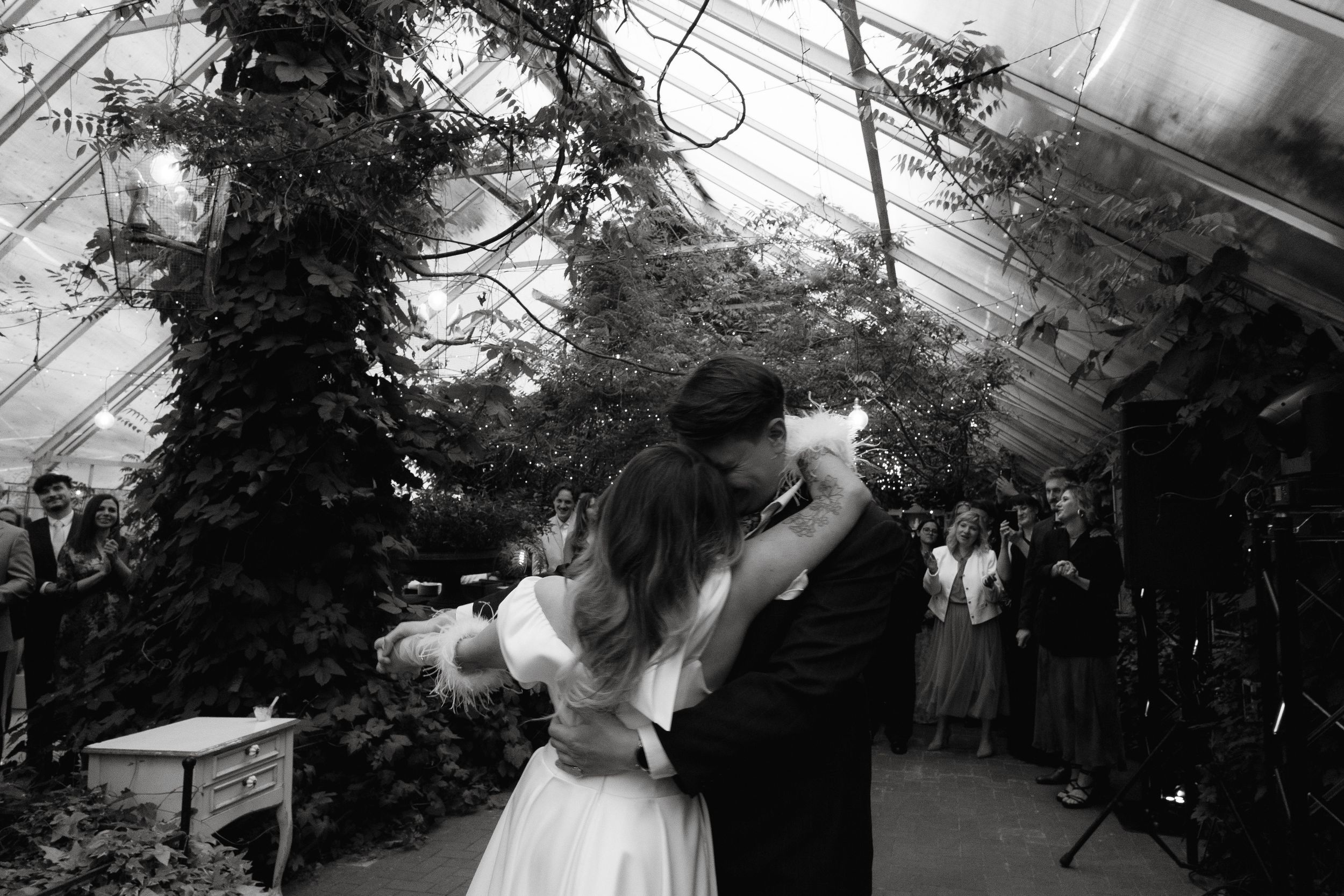 A couple shares their first dance in an intimate greenhouse setting with twinkling lights above.