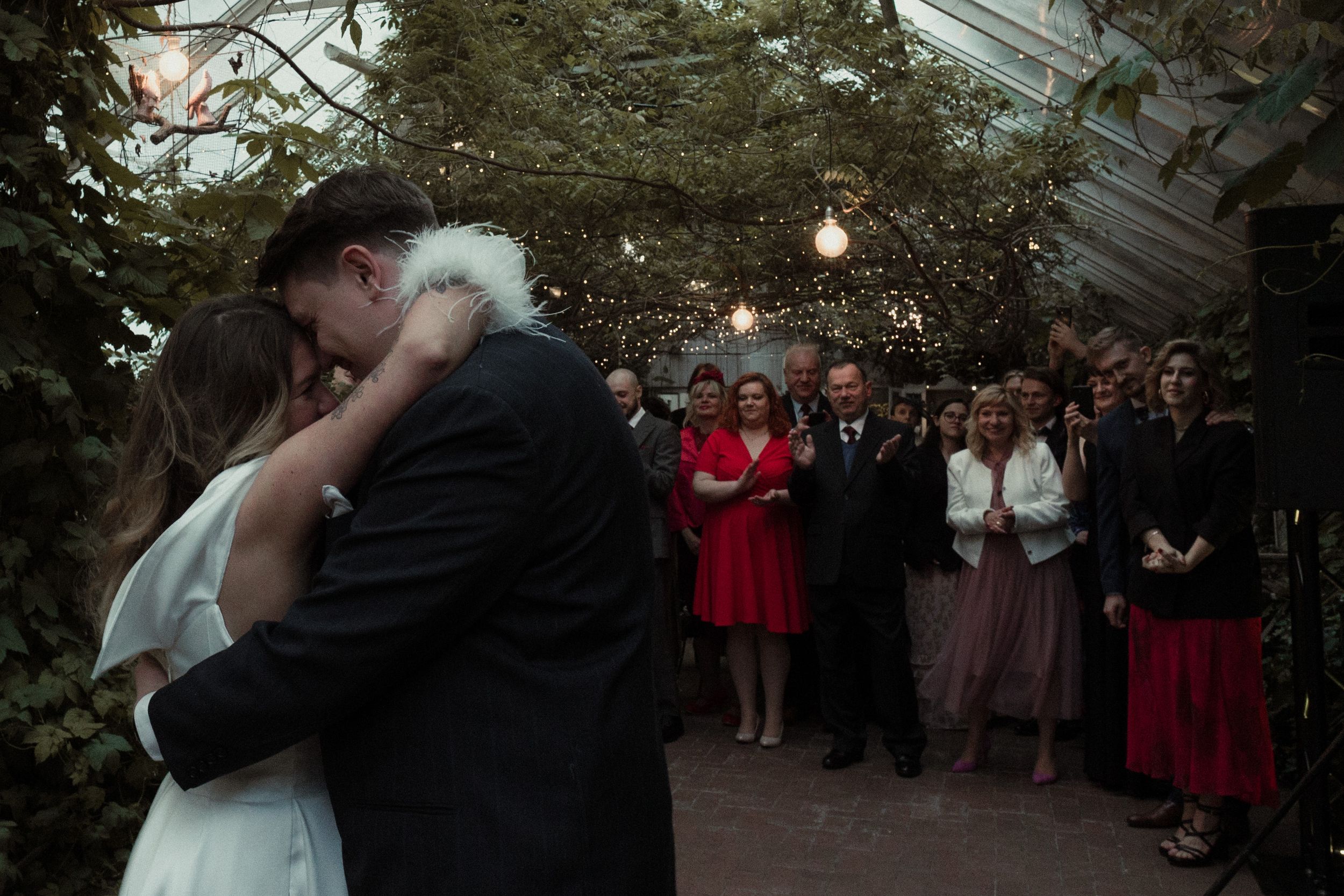 A couple shares their first dance as newlyweds while wedding guests look on in a romantically lit garden setting.