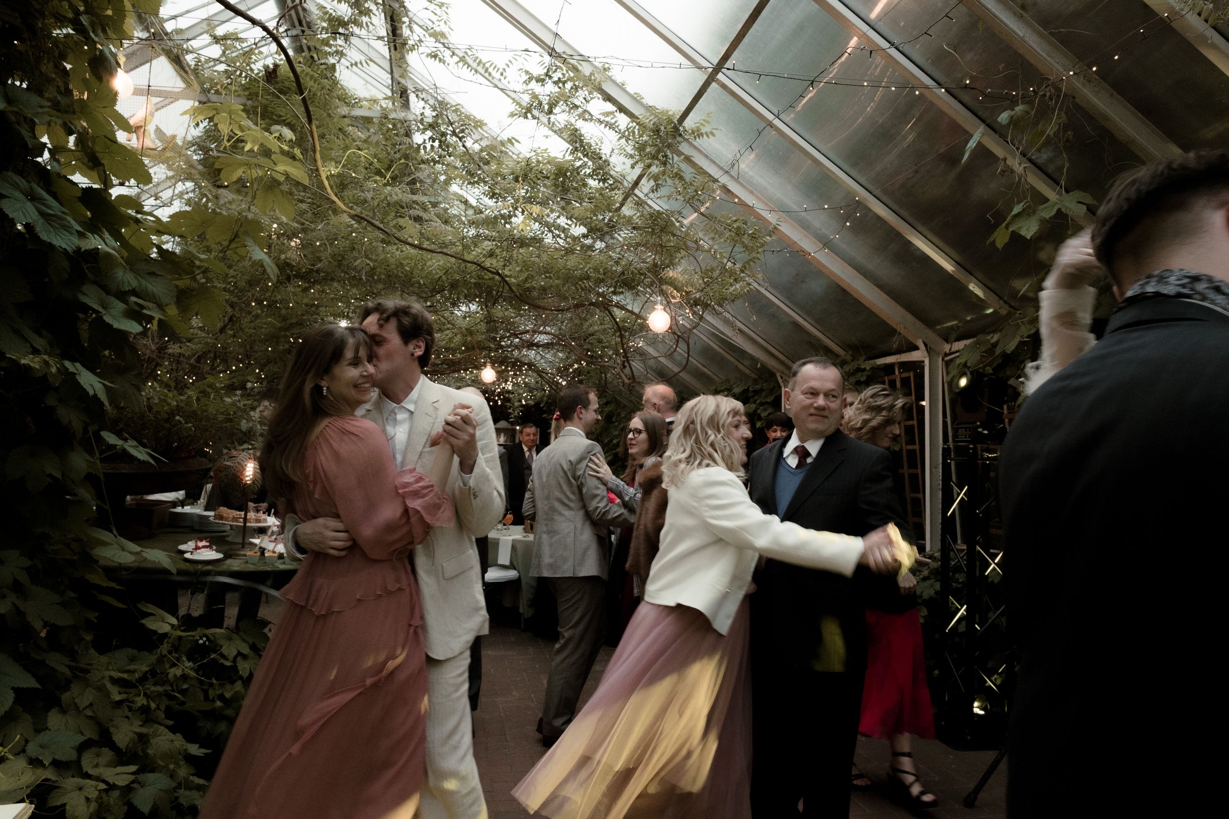 People dancing and celebrating at an indoor greenhouse wedding reception.