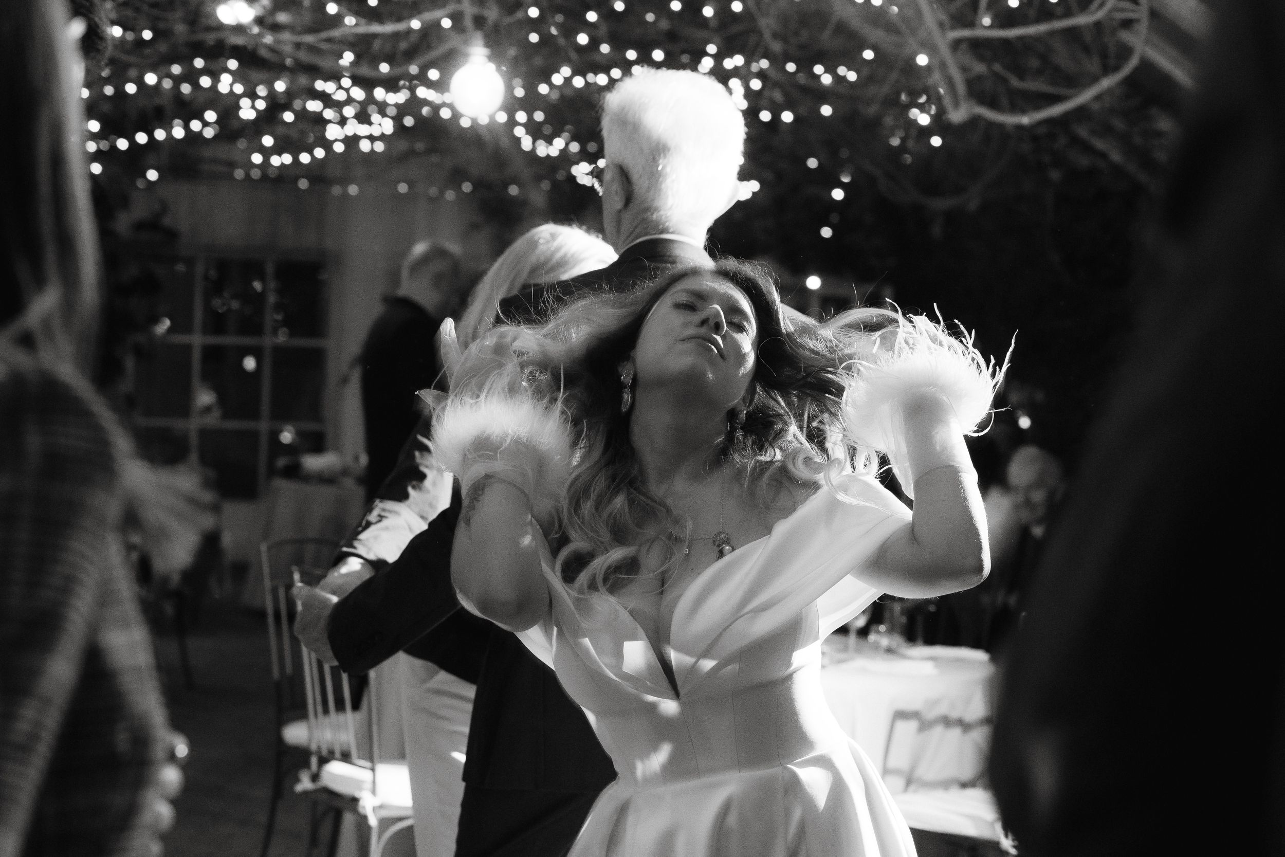 Wedding guests dancing and celebrating under sparkling lights at an indoor reception venue.