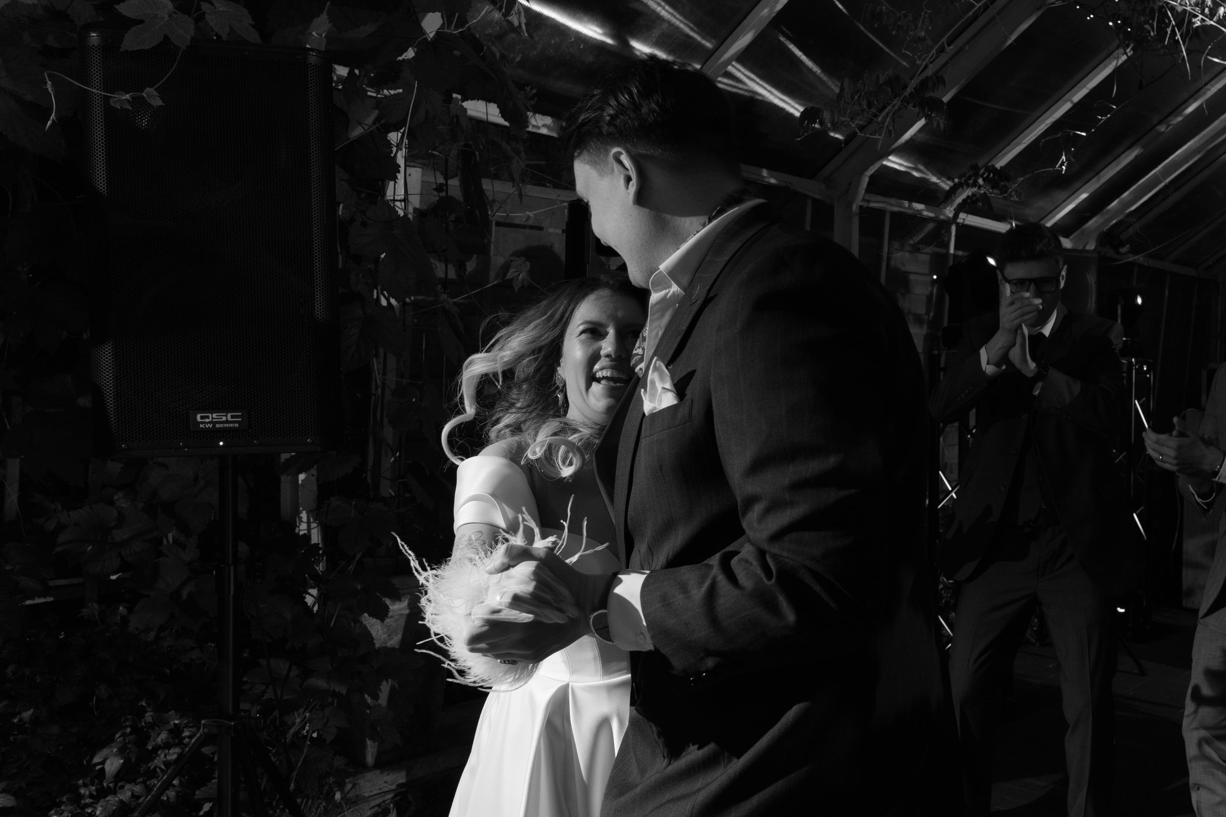 Black and white photo of a couple dancing together in an intimate indoor setting with overhead lighting.