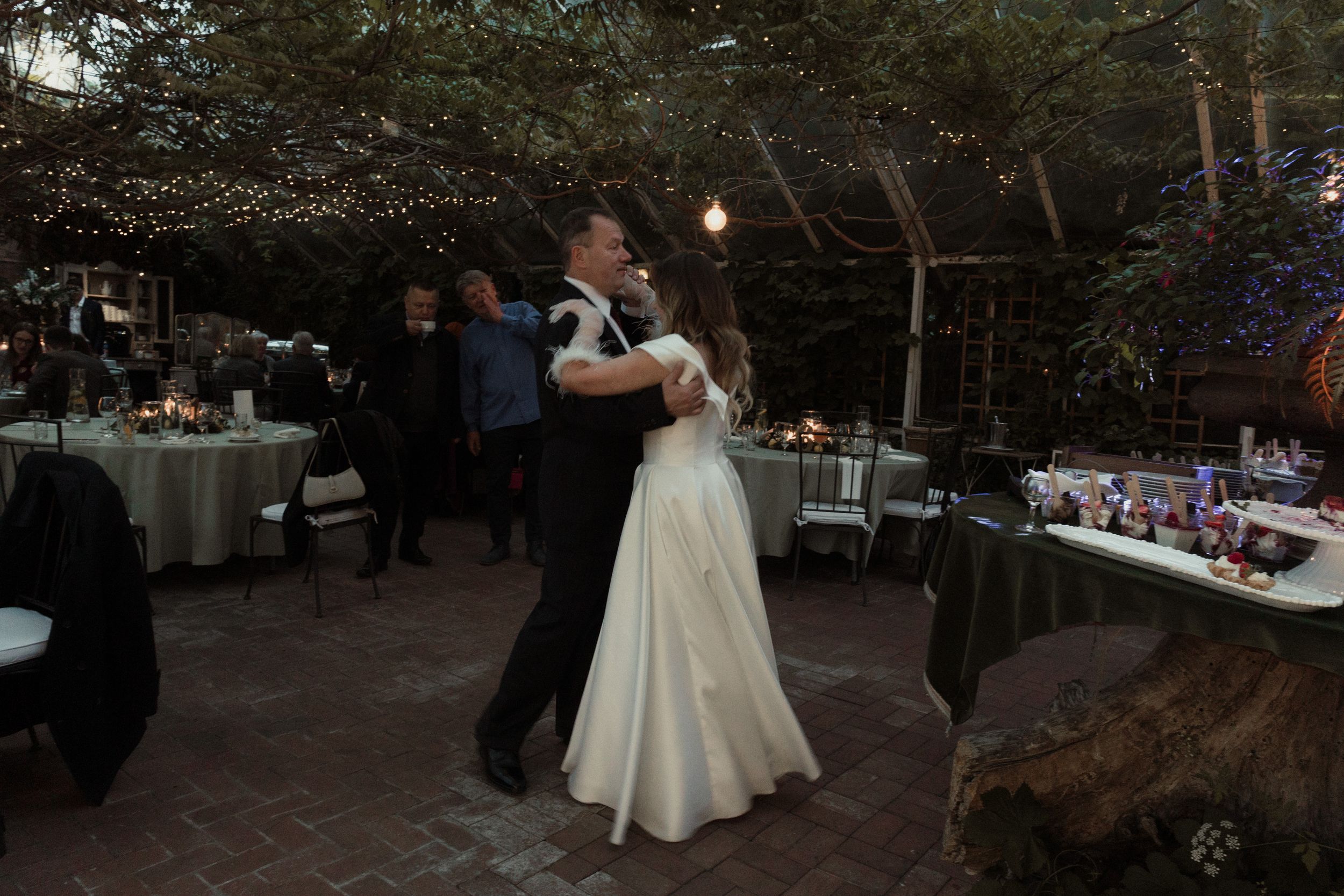 Wedding reception dance at an outdoor venue with ambient lighting and table settings.