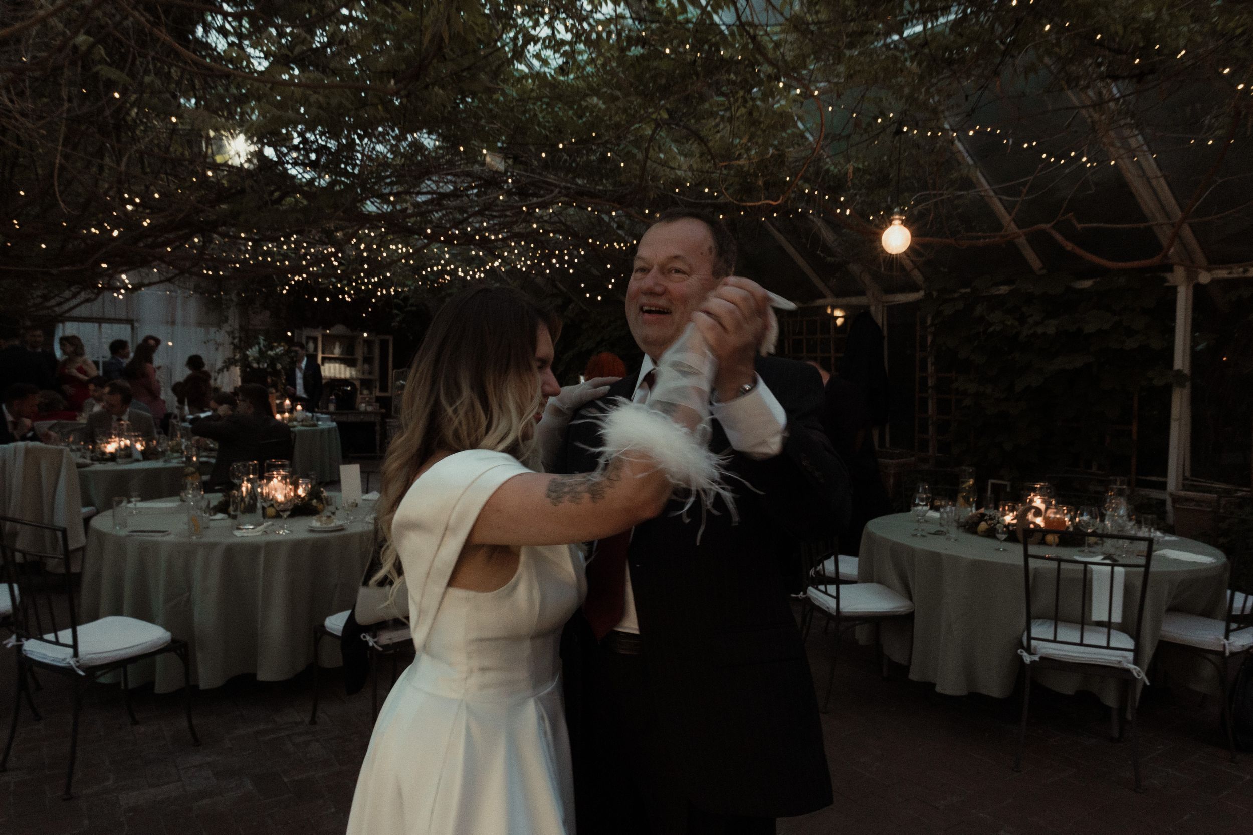 Couple shares a romantic dance at dusk under string lights at an outdoor reception.