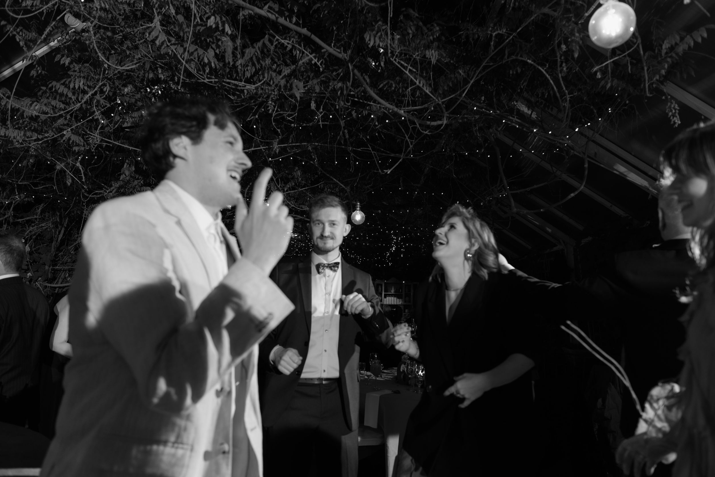 Party guests dancing enthusiastically under string lights at a nighttime celebration.