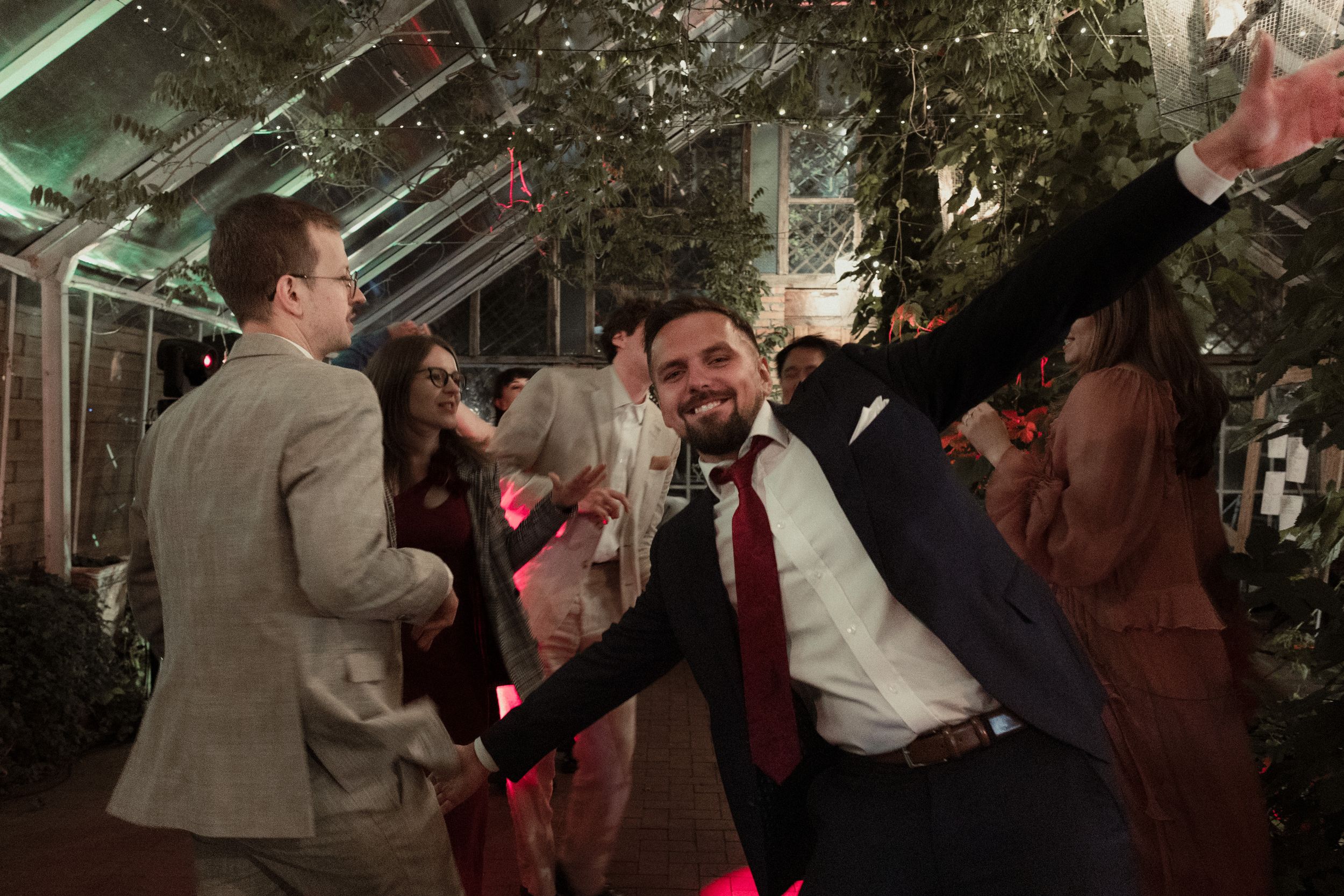 Guests enjoying themselves at a dimly lit indoor wedding celebration with decorative lights.