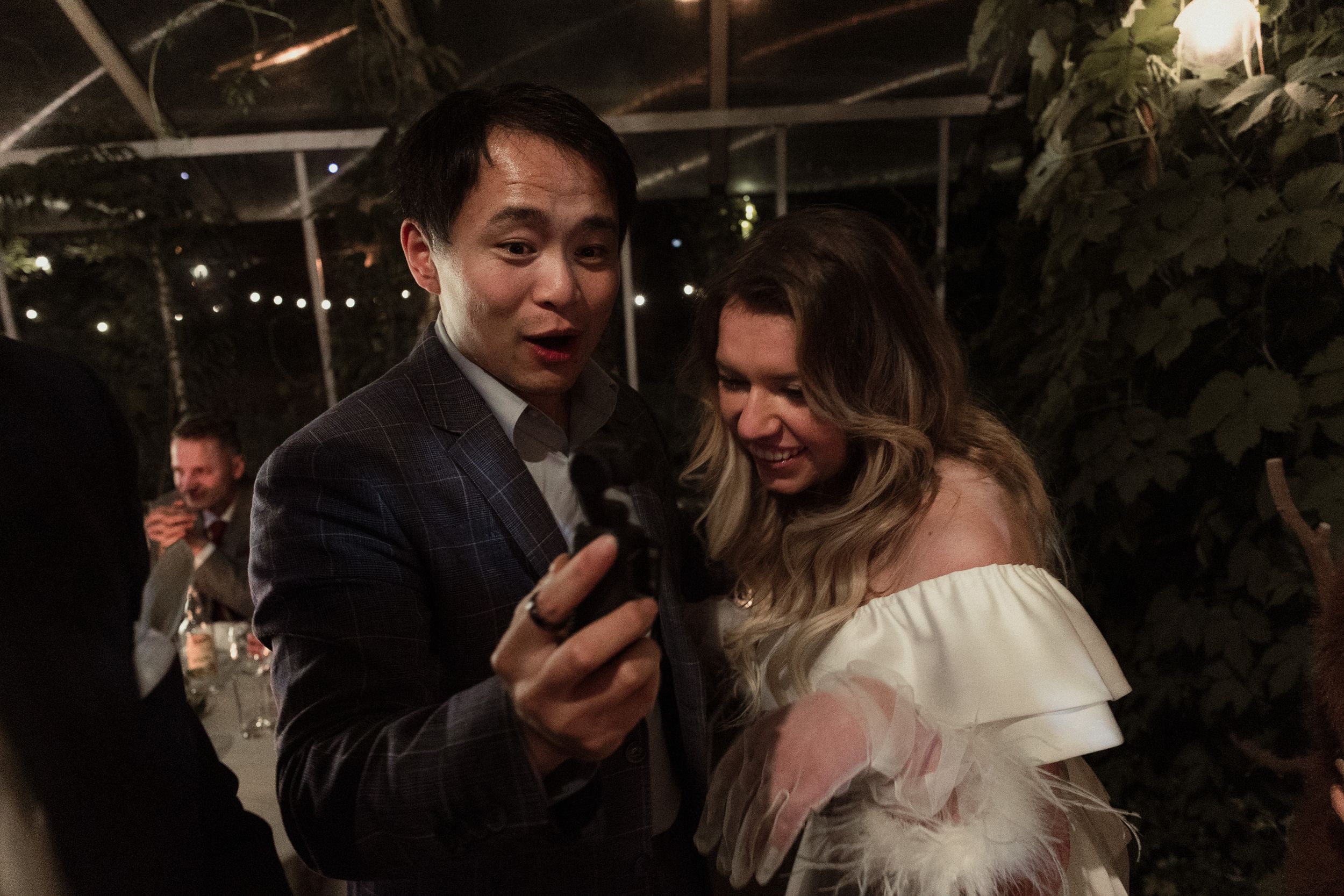 Wedding guests dancing and socializing at an evening reception under decorative lighting.