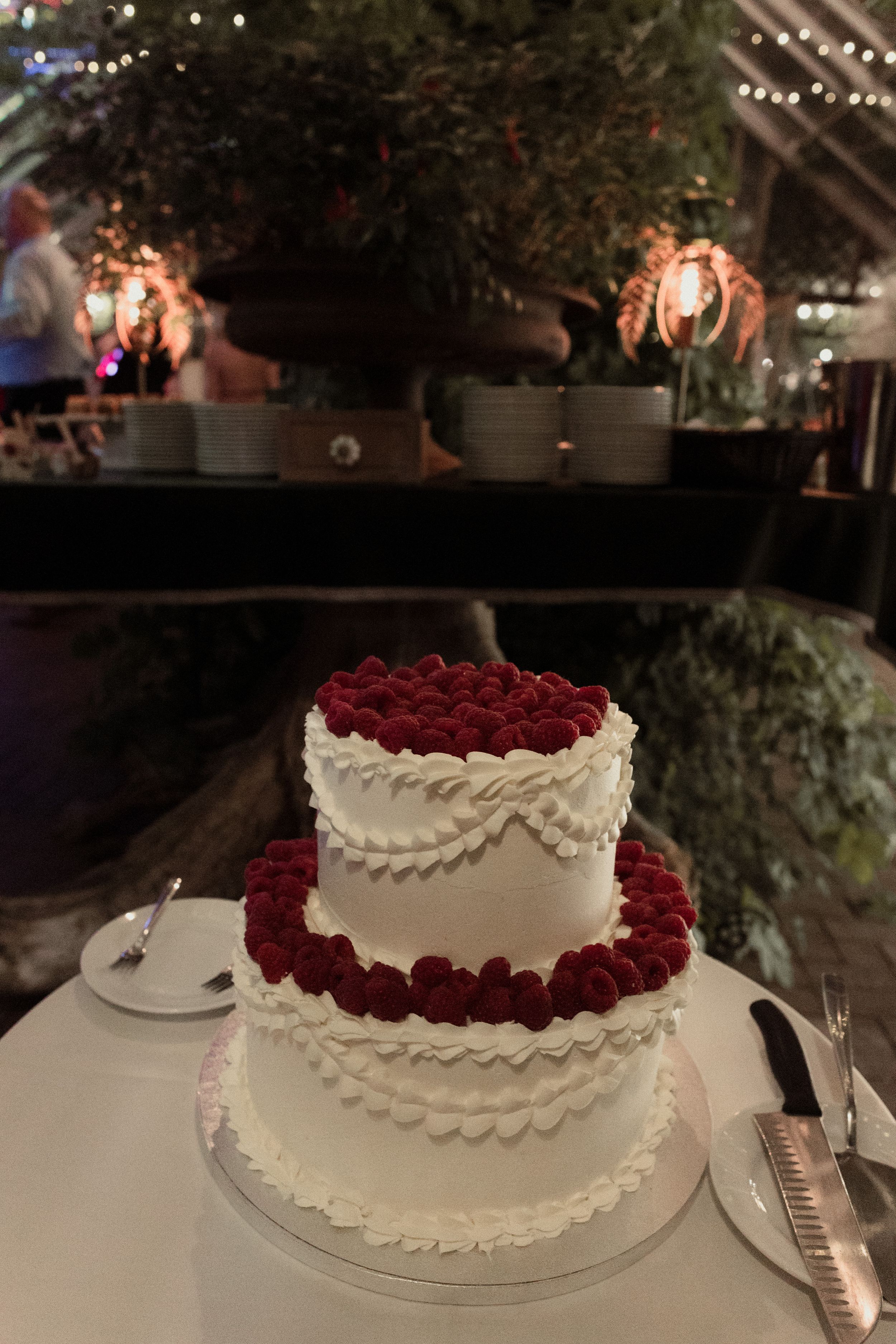 Elegant two-tier white wedding cake decorated with red roses on display at reception.