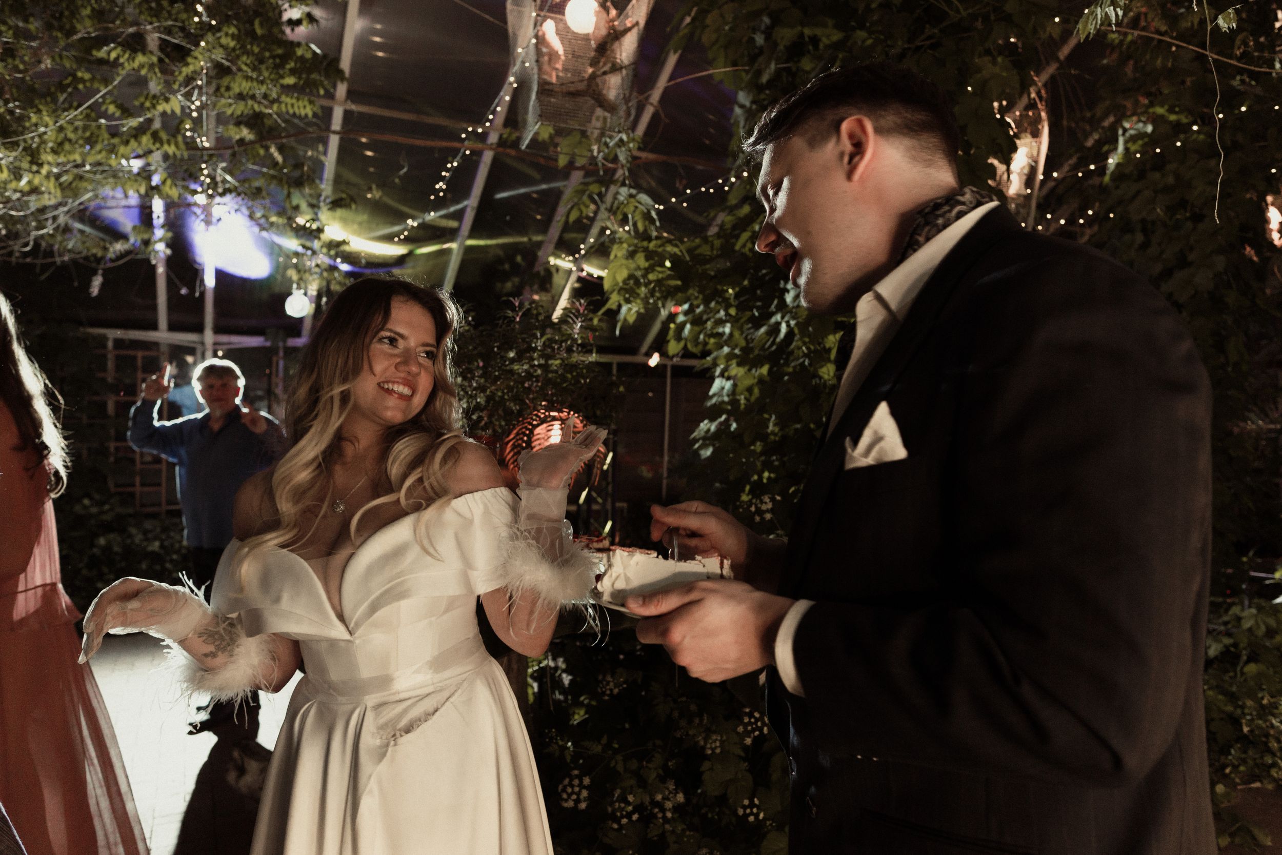 Wedding celebration with guests dancing under greenhouse lighting and foliage.