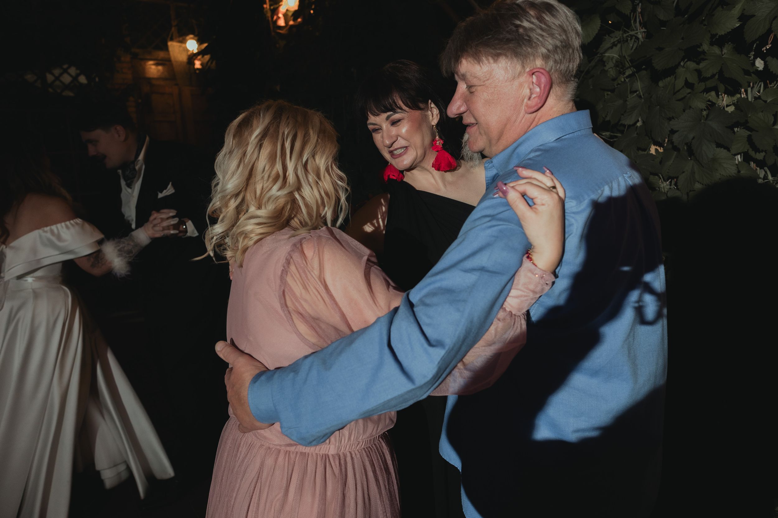 Couples dancing together at an evening celebration with string lights overhead.