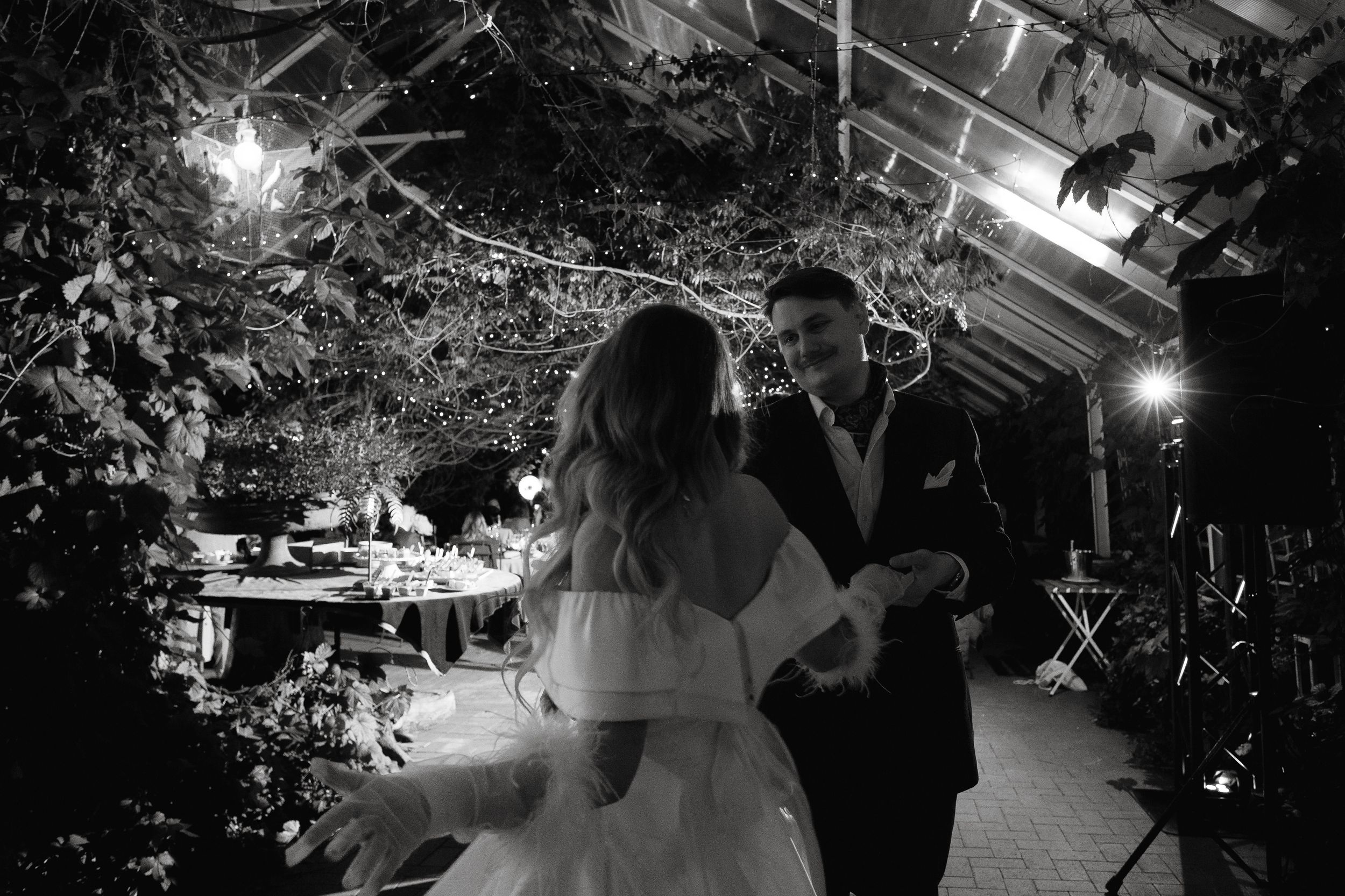 Evening dance celebration in a greenhouse venue with overhead lighting.