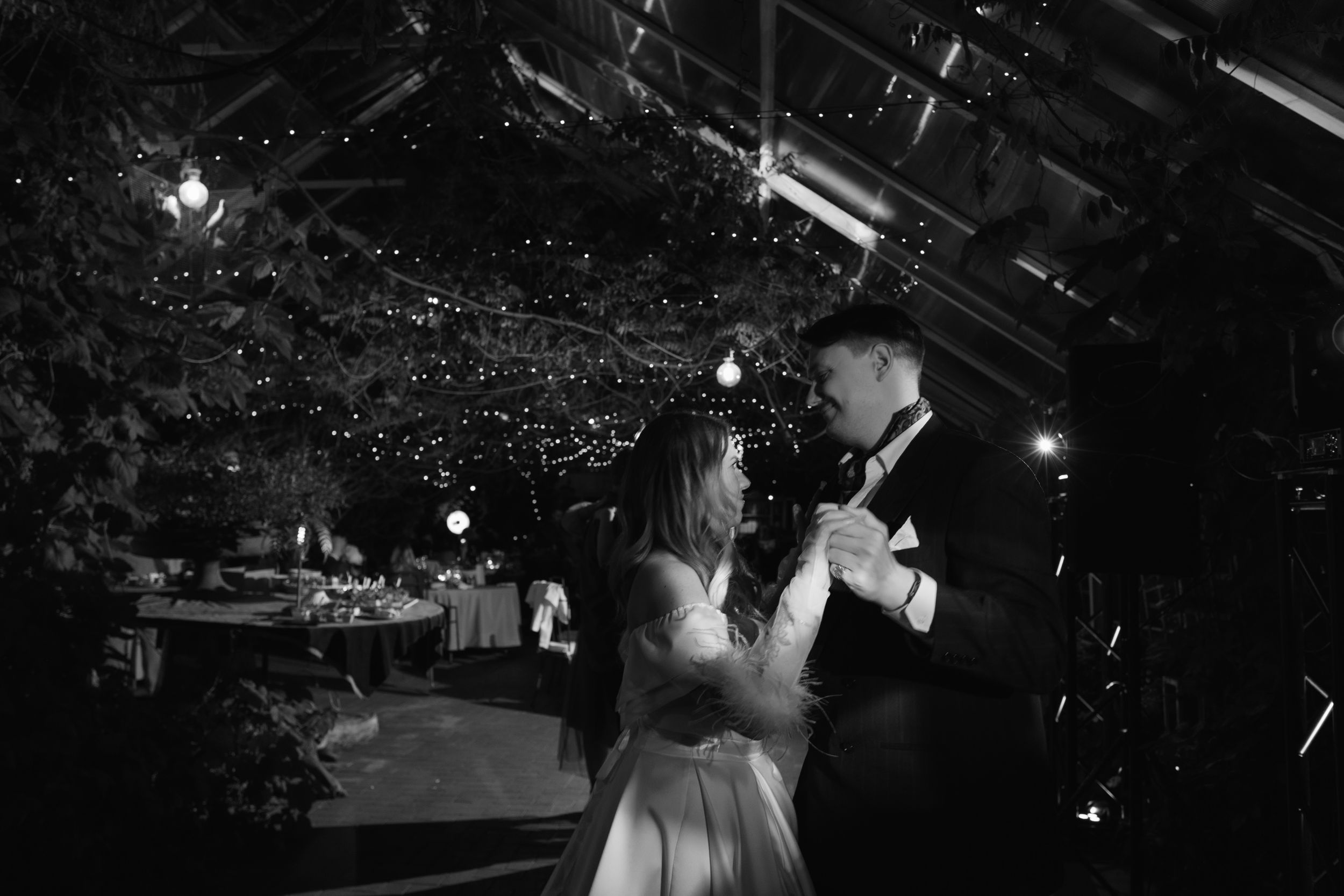 Black and white photo of a couple dancing under twinkling greenhouse lights.