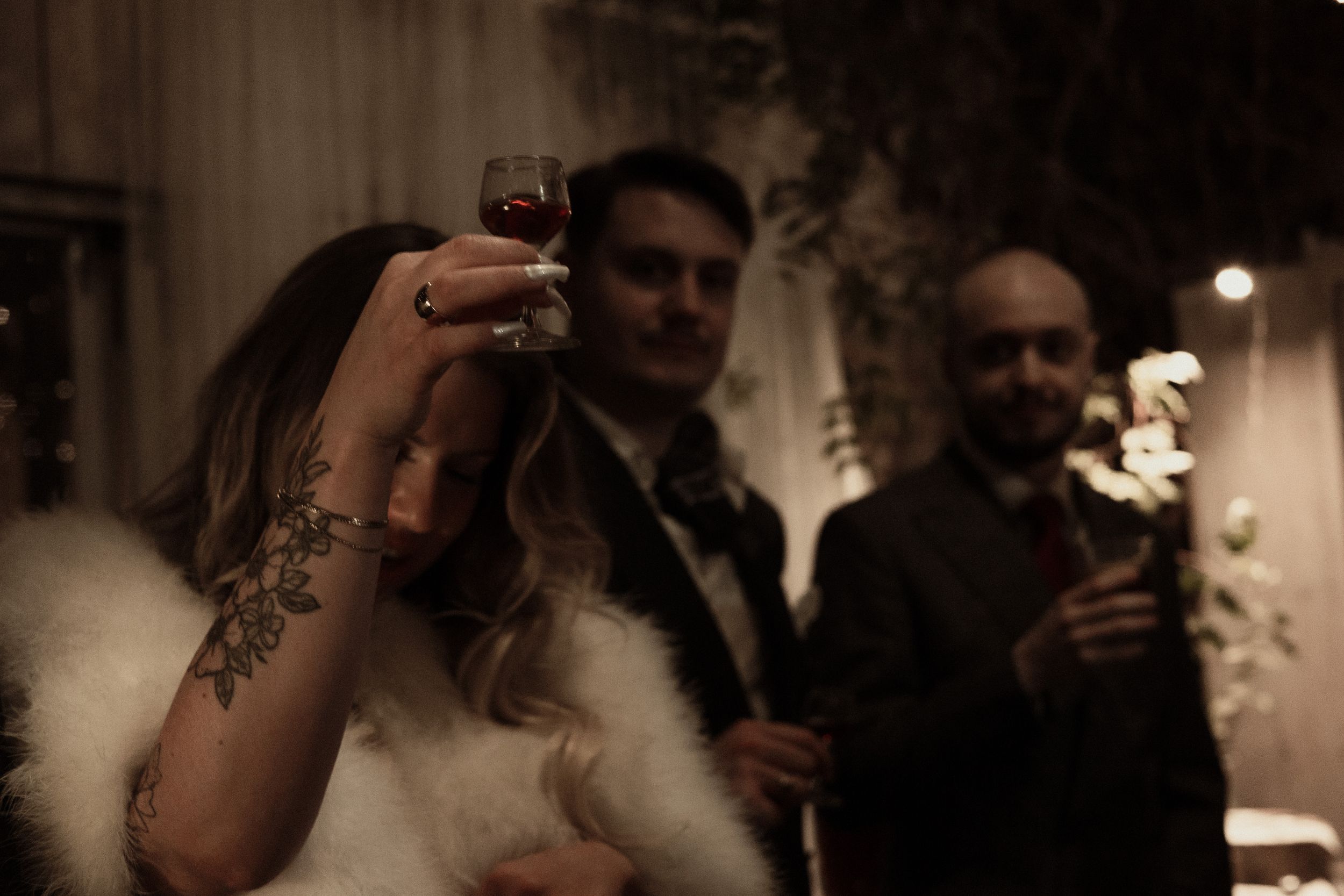 People holding wine glasses at an elegant evening event in a dimly lit room with atmospheric lighting.