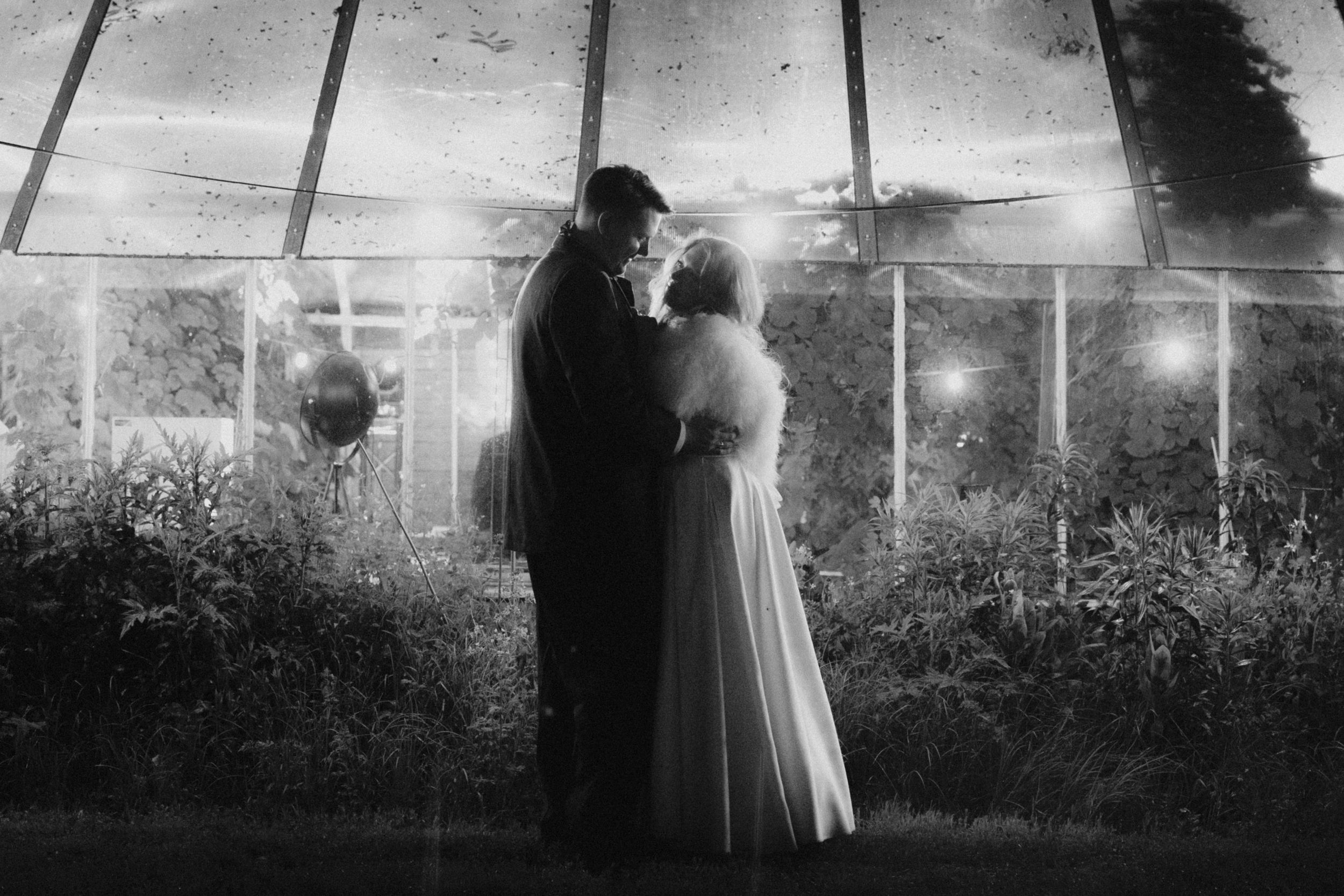Black and white panoramic shots of a couple in formal attire standing among garden landscaping.