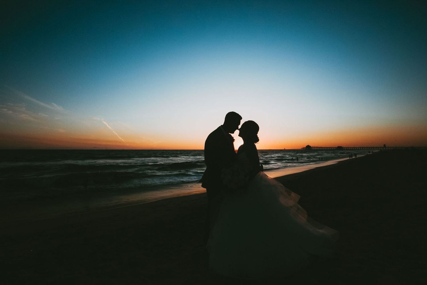 Silhouettes of couple embracing on a beach at sunset with dramatic orange sky and dark foreground.