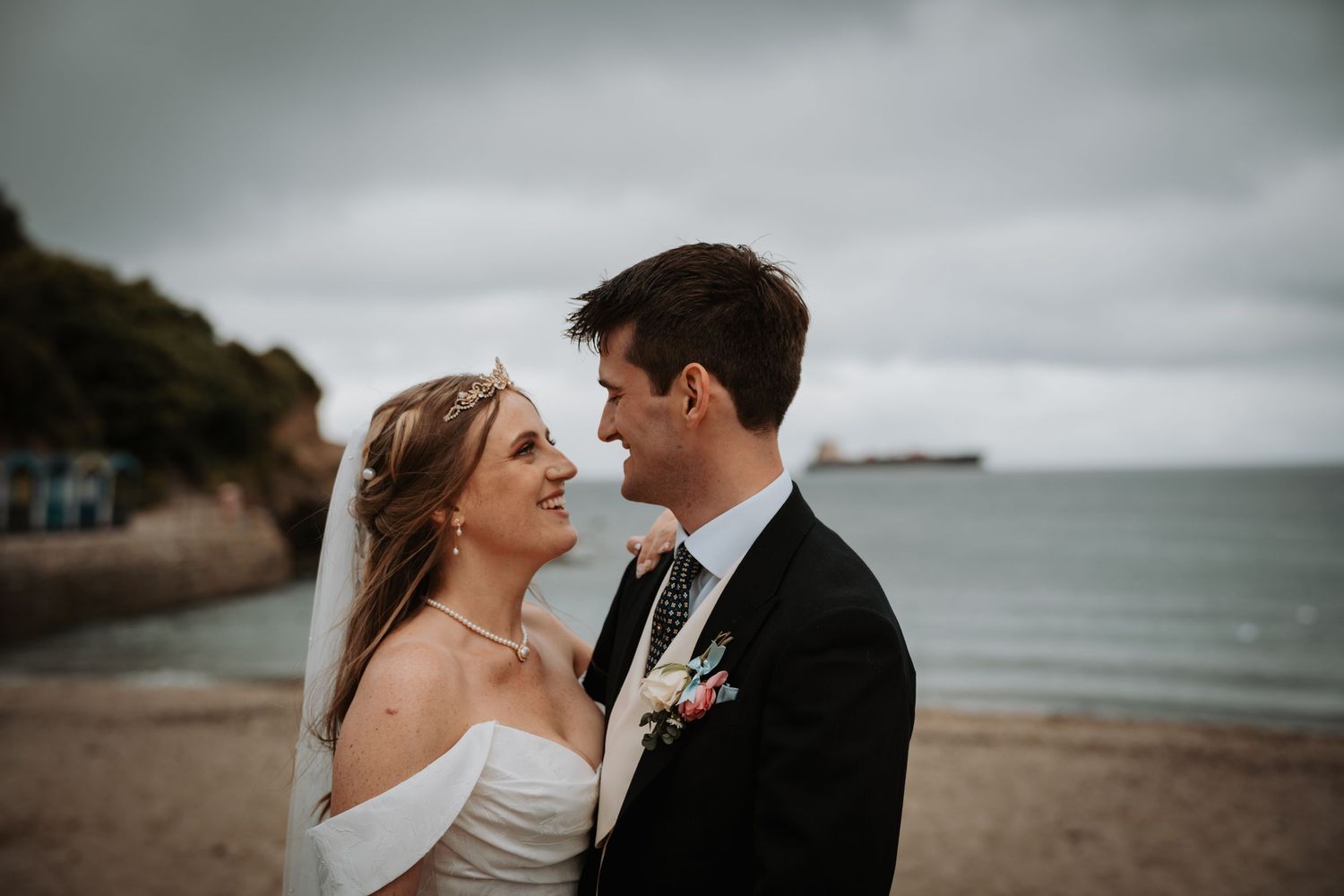 Two people sharing a romantic moment on an overcast beach during what appears to be a wedding day.
