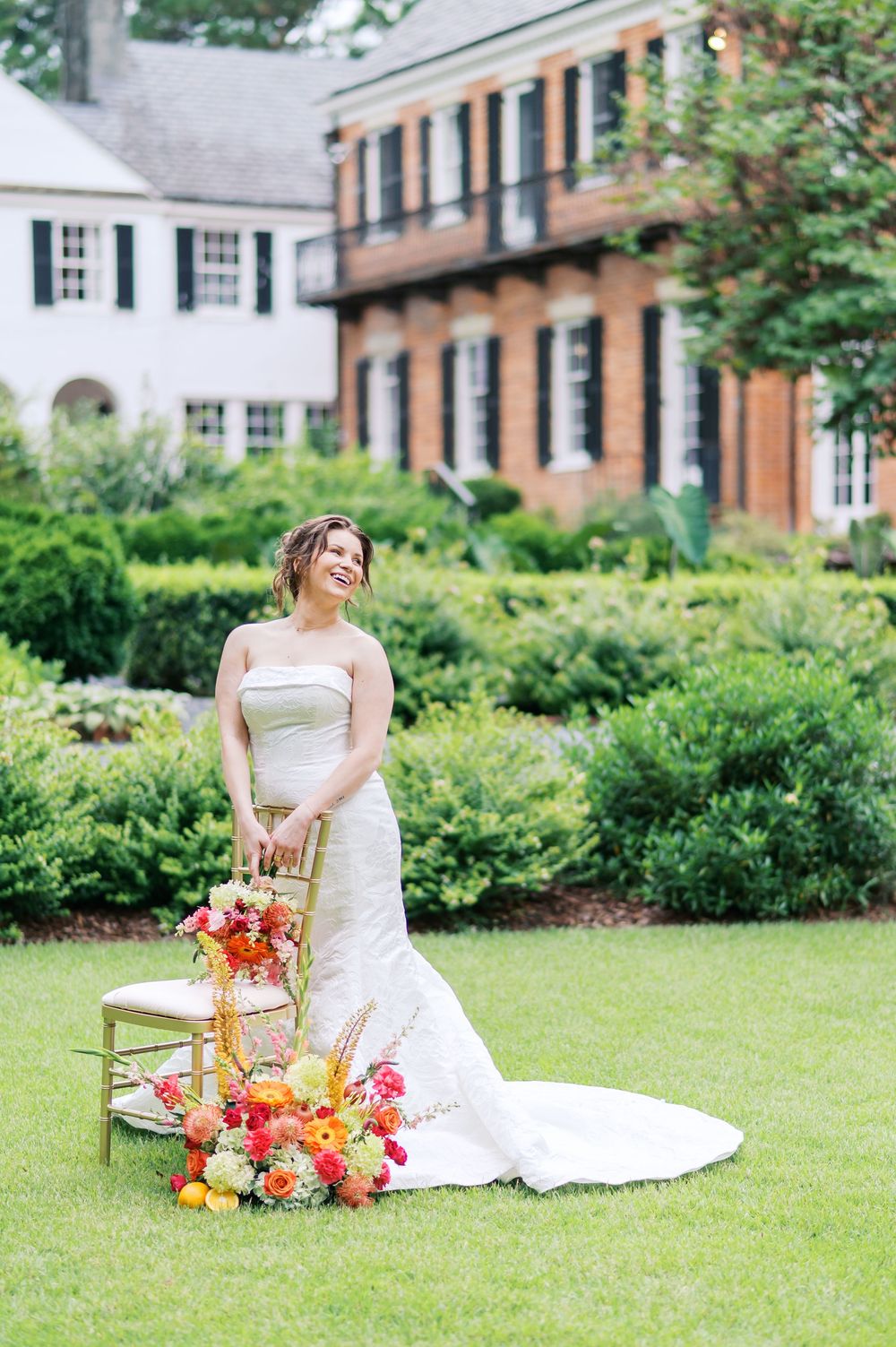 Elegant bride in white gown poses with vibrant orange and pink floral arrangements on a lush green lawn at Weymouth in Moore County NC