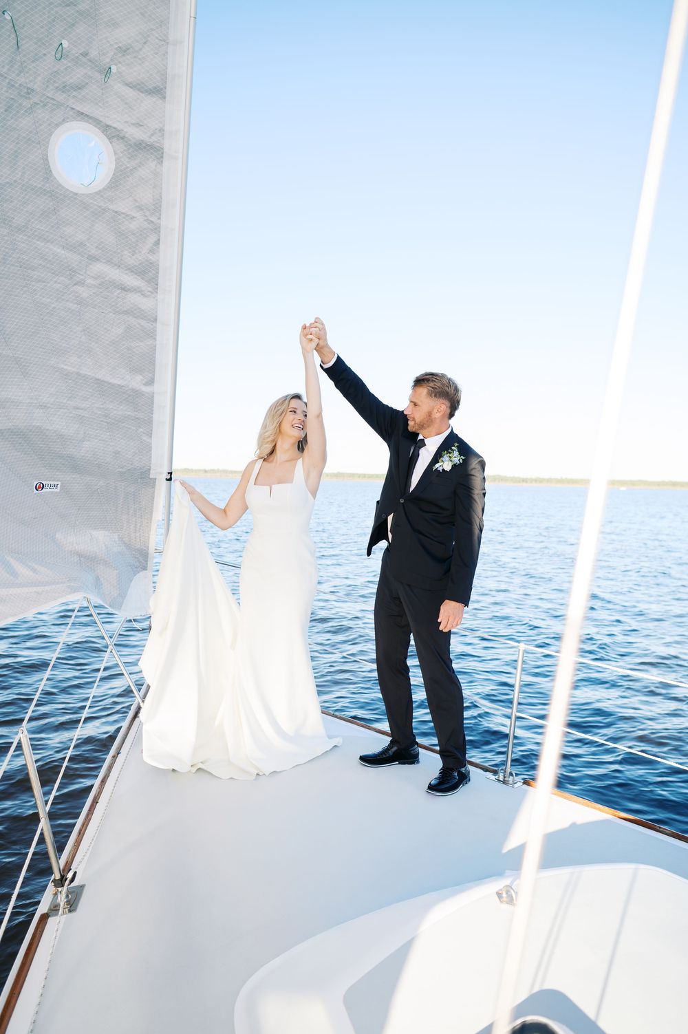 A couple in wedding attire dances together on a boat deck with the ocean visible in the background. Photograph by Fayetteville Photographer