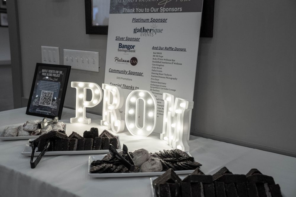 Illuminated marquee letters spelling PROM against a white wall with decorative elements.
