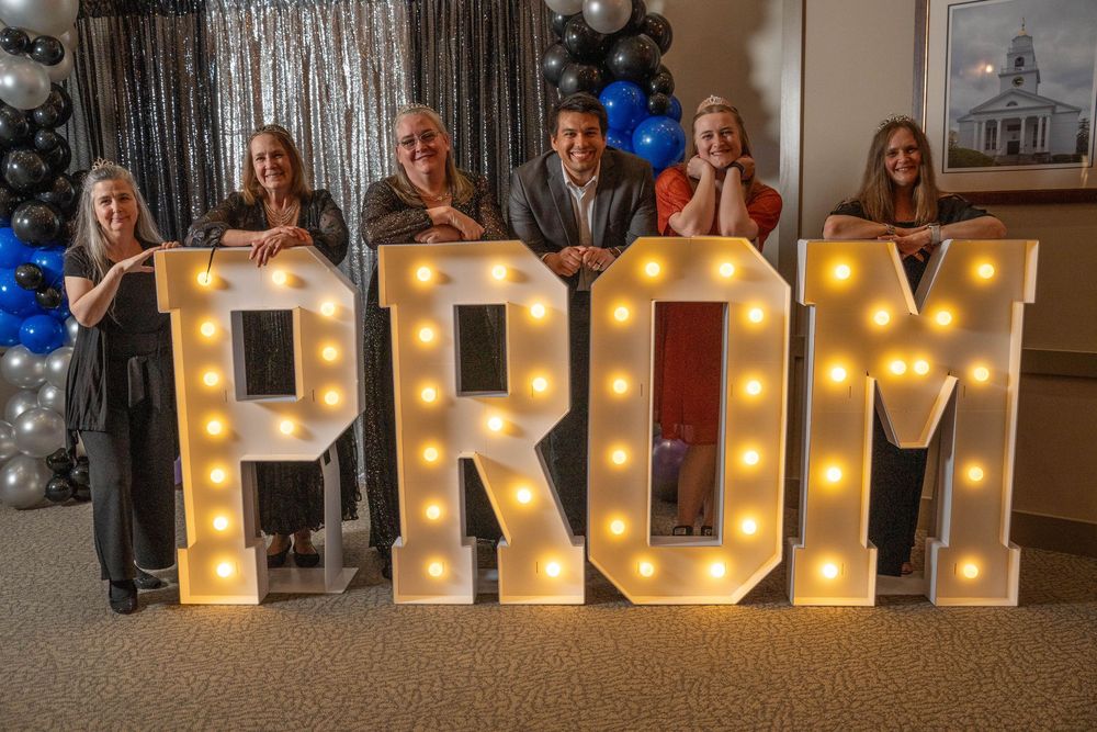 Glowing gold marquee letters arranged against a silver tinsel backdrop at an event.