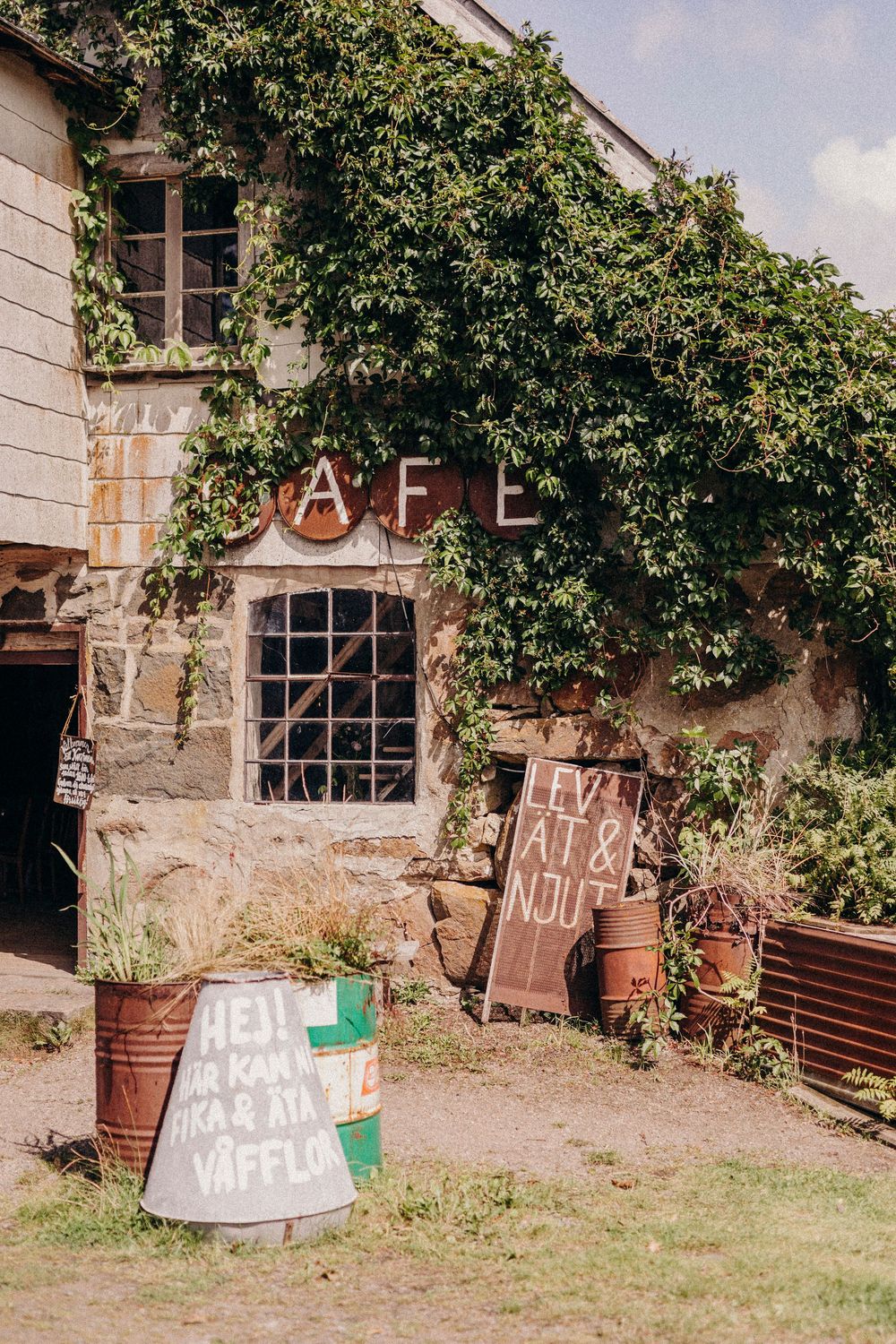 Rustic farm building exterior with ivy-covered walls and potted plants on a grassy yard.