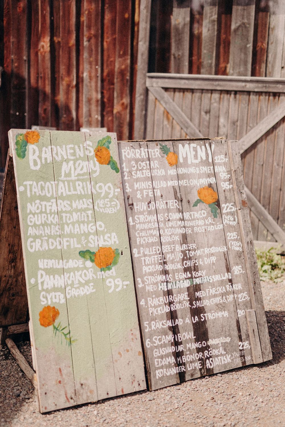 Rustic wooden menu boards displaying restaurant specials with orange citrus fruit illustrations against a weathered barn wall.