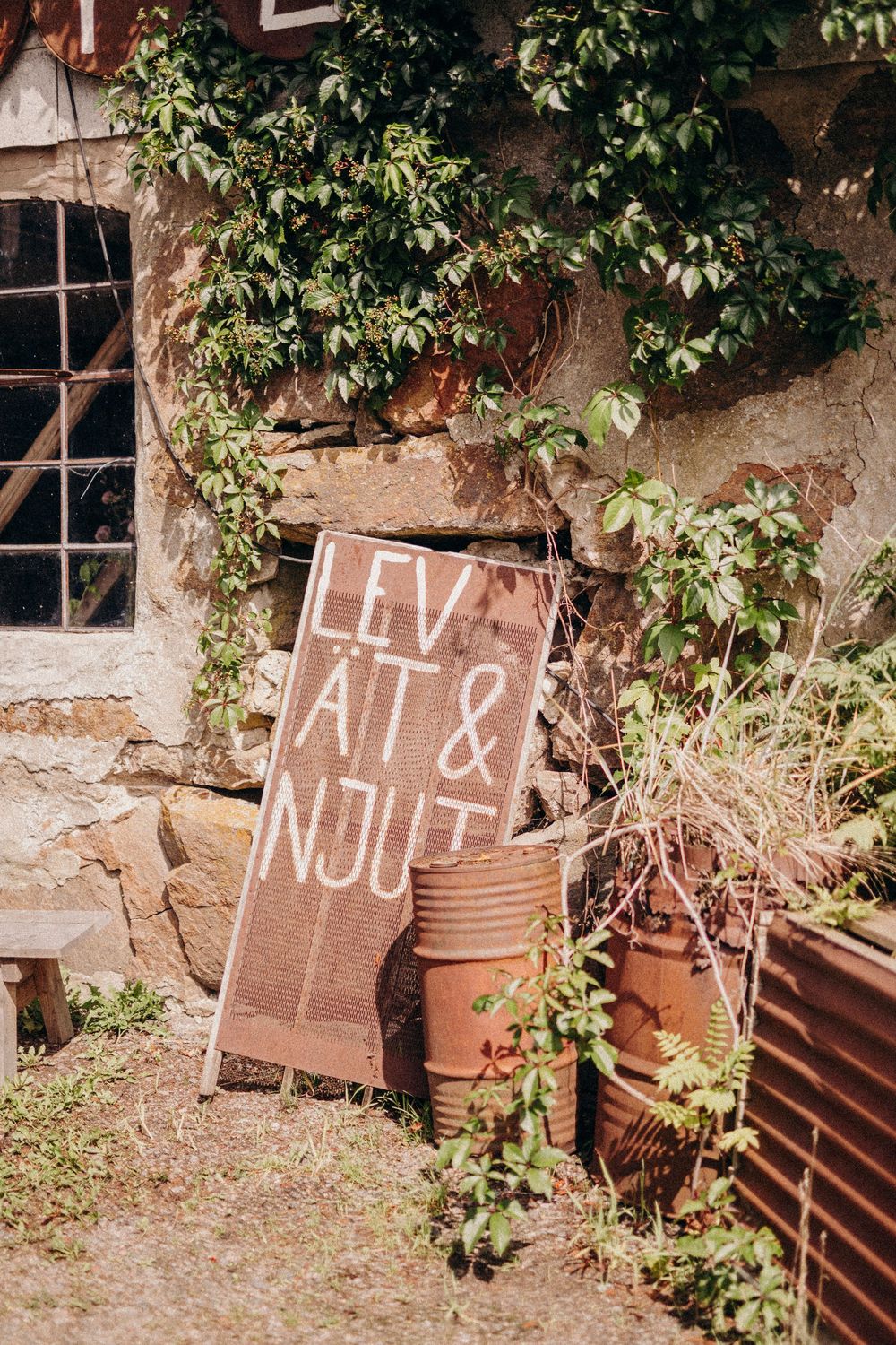 Rustic wooden signs with lettering mounted against stone wall with climbing vines and foliage.