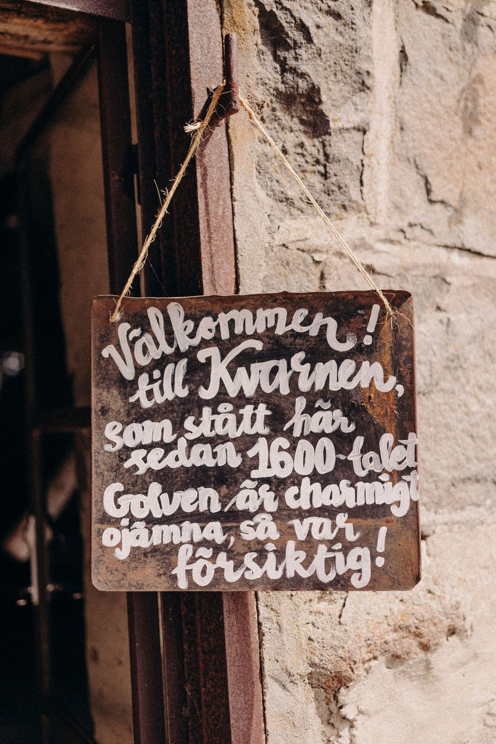 A rustic wooden sign with Swedish text 'Valkommen till Kvarnen' hangs on a stone wall.