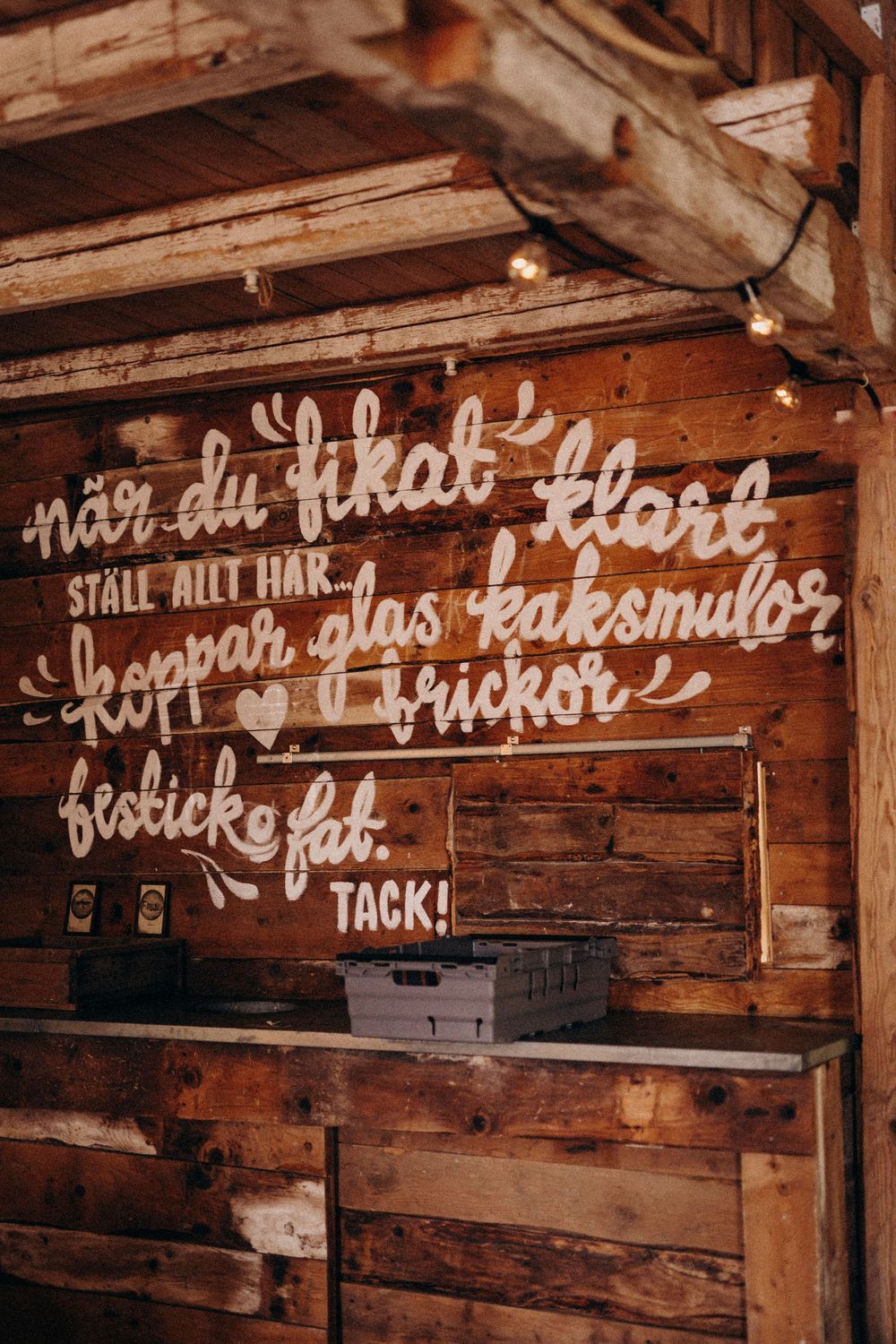 Handwritten text in white paint on weathered wooden beams creates rustic wall signage.