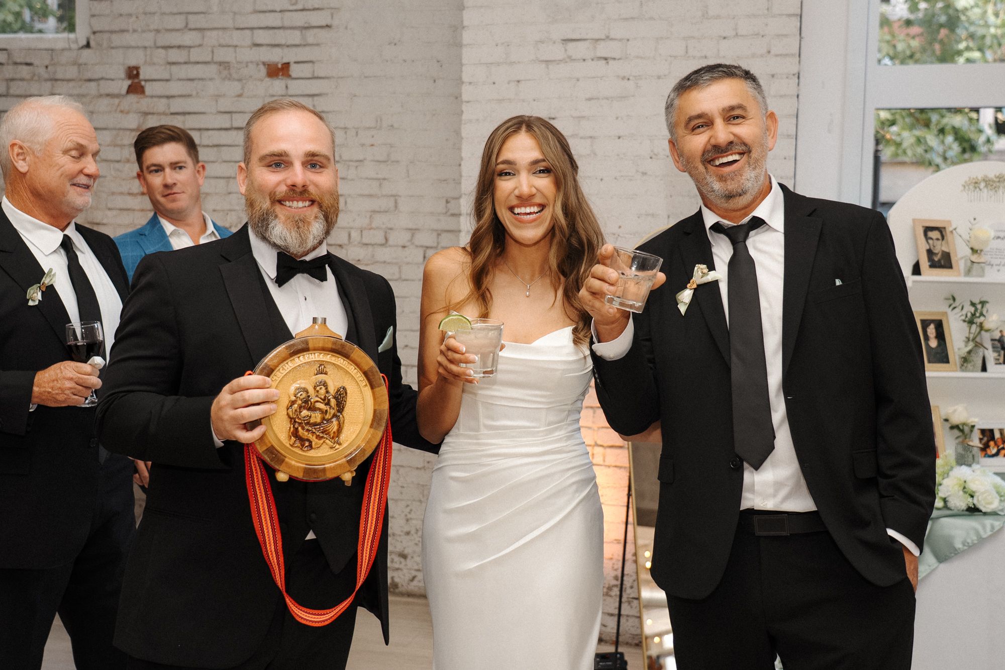 A celebratory wedding reception moment with guests laughing and sharing champagne at an elegant white-themed venue.