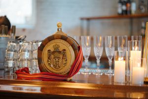 Ornate glass cognac bottle with royal crest sits beside elegant champagne flutes on wooden bar counter.
