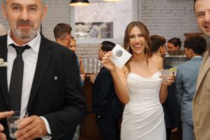 Wedding party in formal attire celebrating on the dance floor at a reception venue with brick walls.