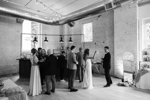 Dance instructor leads couples in learning ballroom dance steps in a bright studio space with exposed brick walls.
