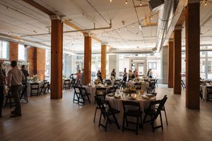 Spacious loft-style event venue with wooden columns, hardwood floors and round dining tables set for a celebration.