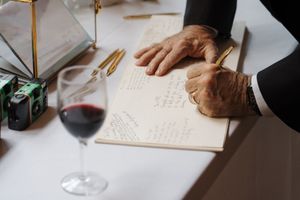 Multiple hands write in a guest book at a wedding reception using elegant gold pens.