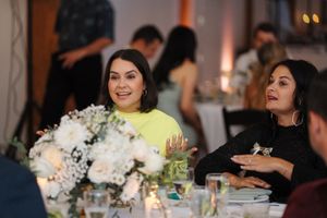 Party guests sit at an elegant dining table with white floral centerpieces and candles at an evening event.