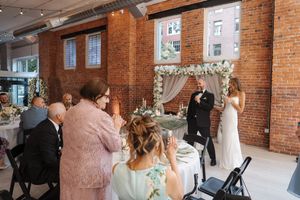 Reception guests mingling inside a rustic brick venue with ornate chandeliers and natural lighting.