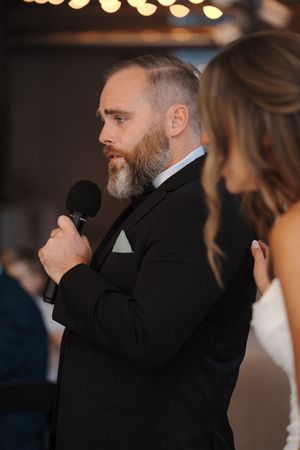 A guest gives a heartfelt speech at an elegant wedding reception with bokeh lights in the background.