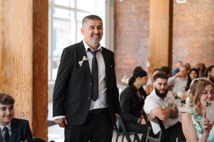 Wedding guests laugh and celebrate during a reception in a rustic brick-walled venue with wooden beams.