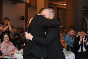 Two people share a tender embrace on the dance floor at an elegant indoor reception event.