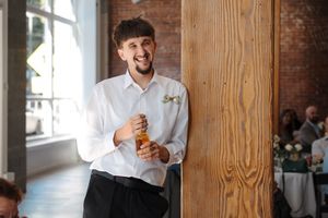 Professional chef in white uniform and cap stands against rustic wood paneling in restaurant setting.